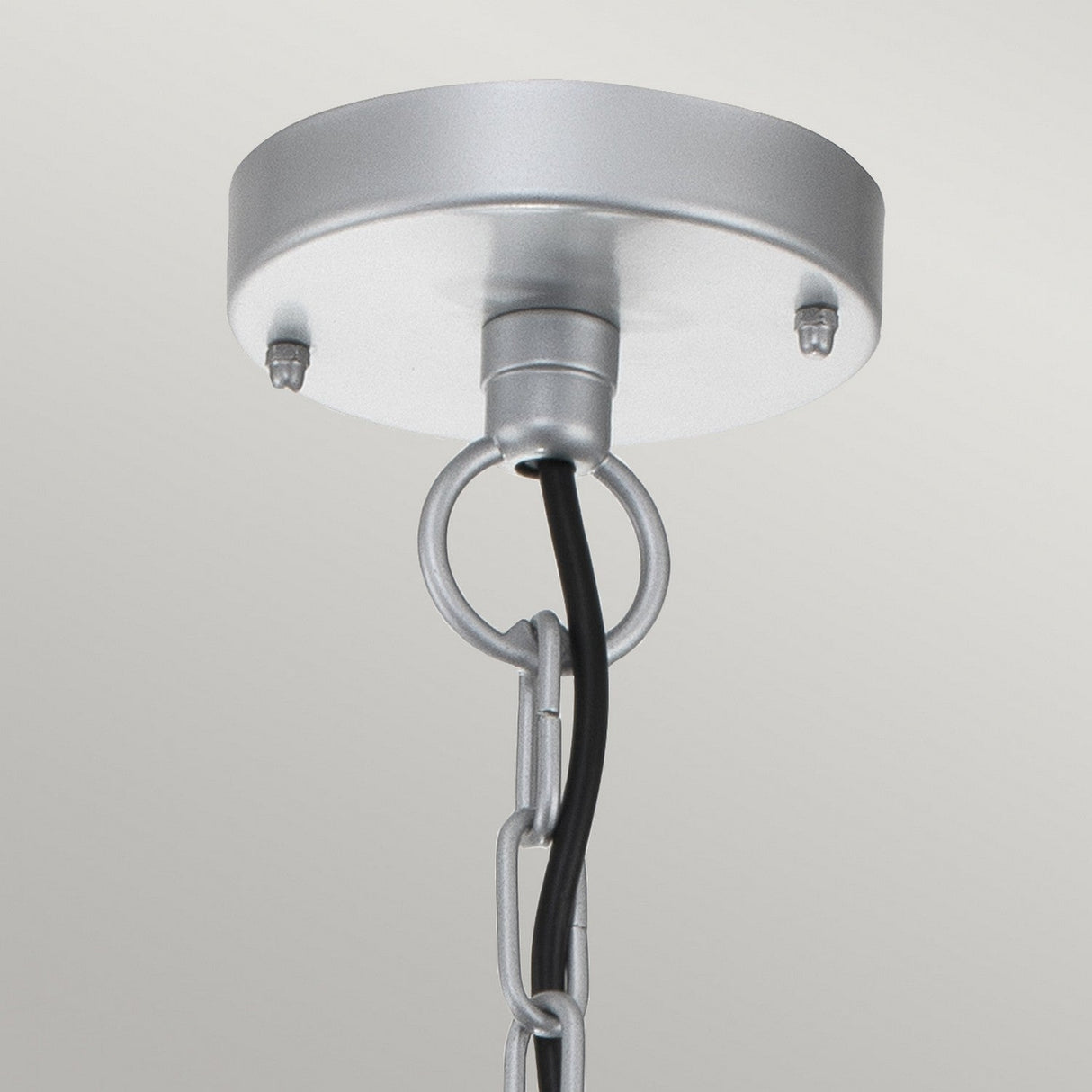 Close-up of the Klampenborg 1 Light Outdoor Chain Pendant in silver, featuring a sleek metal chain that embodies Scandinavian Minimalism. A black electrical cord threads through the center, connected to a round, stainless steel base secured with two screws against a plain backdrop.