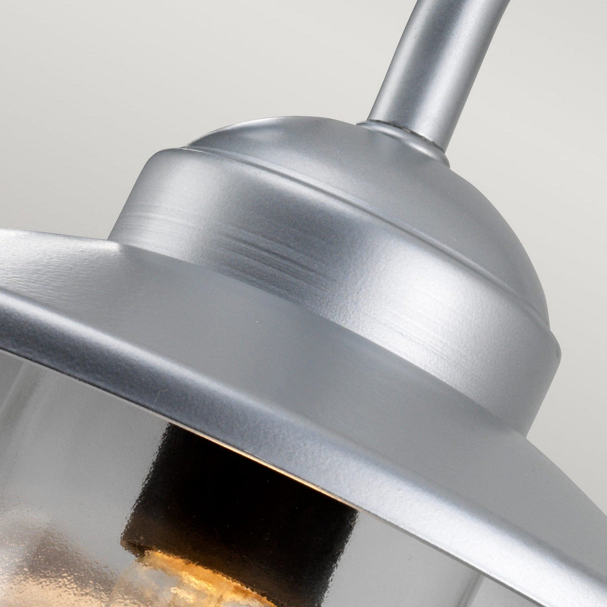 Close-up of the Klampenborg 1 Light Outdoor Wall Light in silver, featuring a modern design. The image showcases the top portion of the fixture, highlighting its smooth metallic surface and the clear glass that encloses the bulb, all protected with an IP44 rating for durability against weather elements.