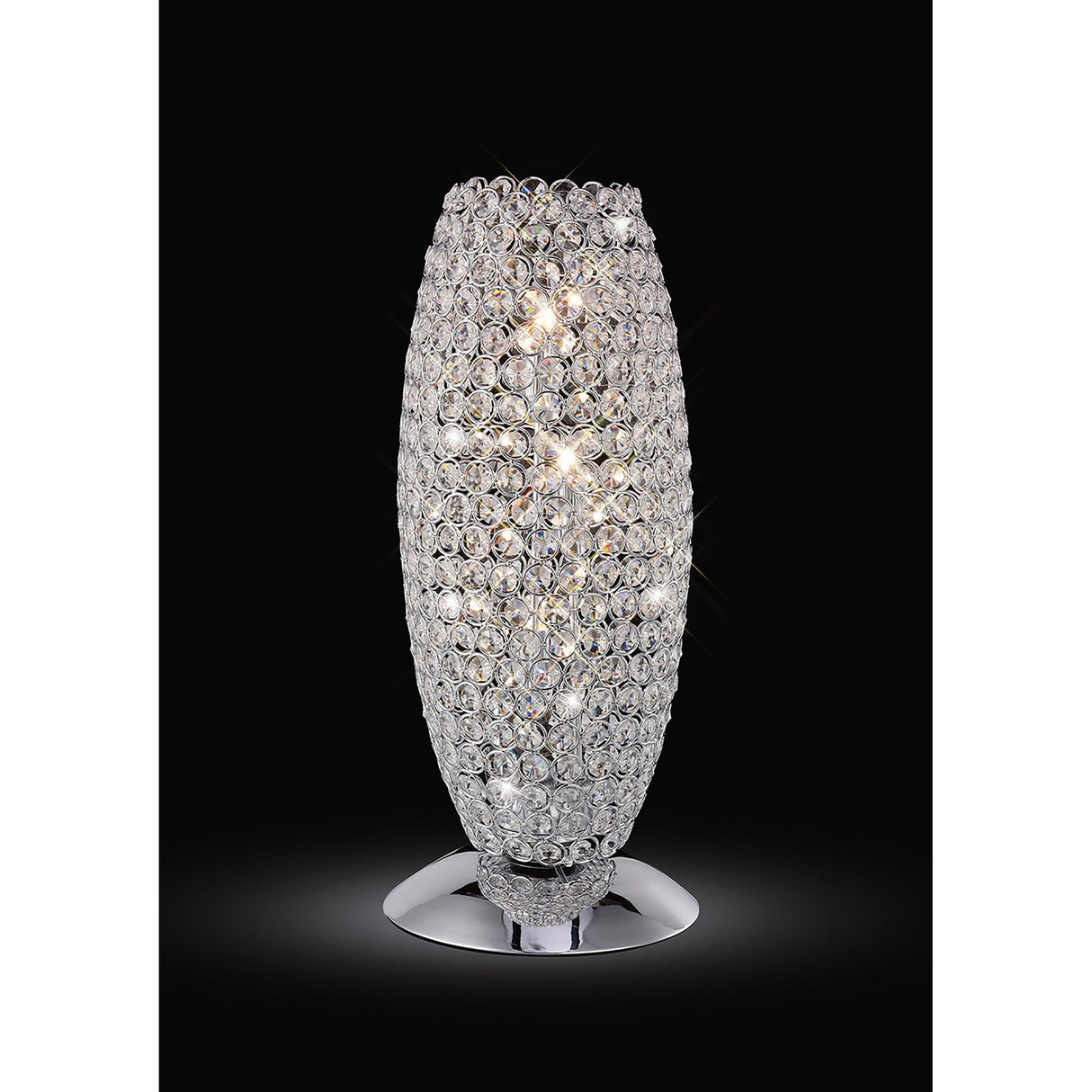 The Kos 3 Light Crystal Table Lamp in polished chrome features a tall oval design with a shiny metal base and circular crystal ornaments, emitting bright, sparkling light—an elegant modern lamp for any setting.
