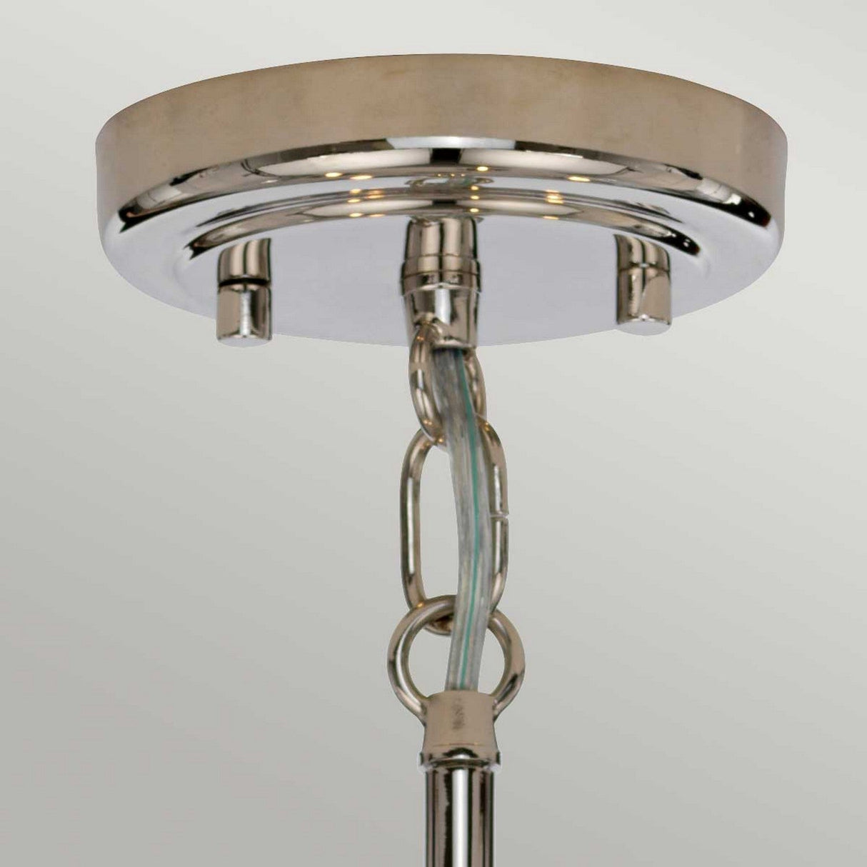 Close-up of the Kula 5 Light Chandelier in polished nickel, showcasing its modern retro style. The fixture is designed with a round base and a hanging chain, featuring visible electrical wiring. Its glass shades enhance the elegant touch of the shiny, reflective finish.