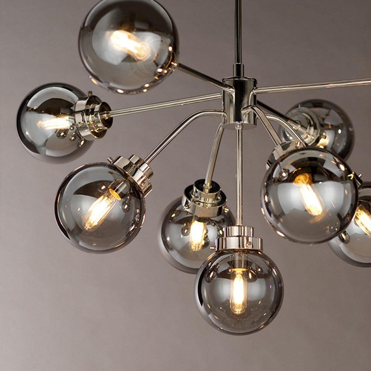 Presenting the Kula 9 Light Chandelier - Polished Nickel, a striking fixture that beautifully merges mid-century modern design with spherical glass bulbs and exposed filaments for a warm glow. Its polished nickel finish and metallic arms extend outward to create an elegant contrast against any neutral backdrop.