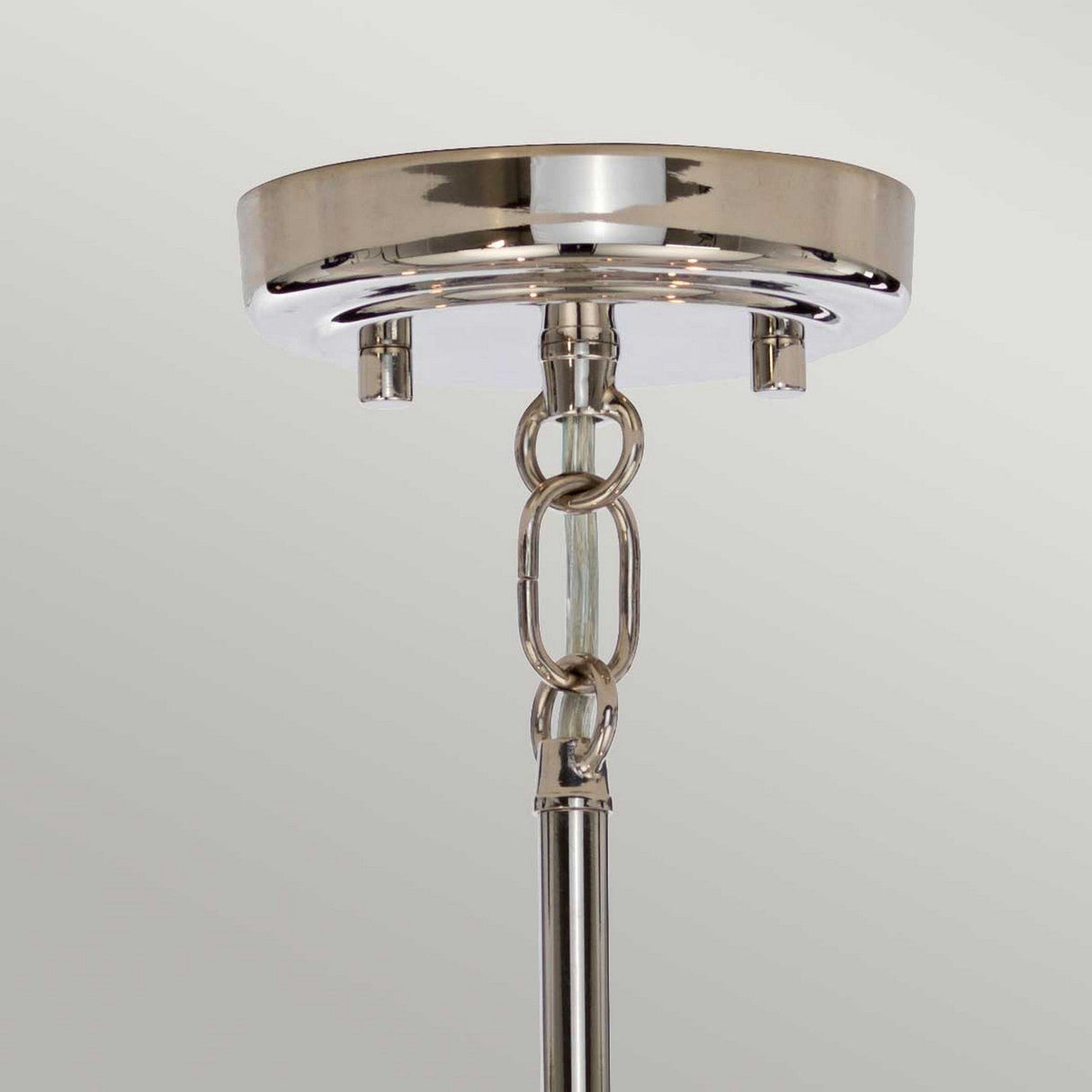 Close-up of the Kula 9 Light Chandelier - Polished Nickel, featuring a polished nickel finish ceiling mount with a linked metal chain detail connected to a hanging rod. The plain light gray background complements its mid-century modern elegance.