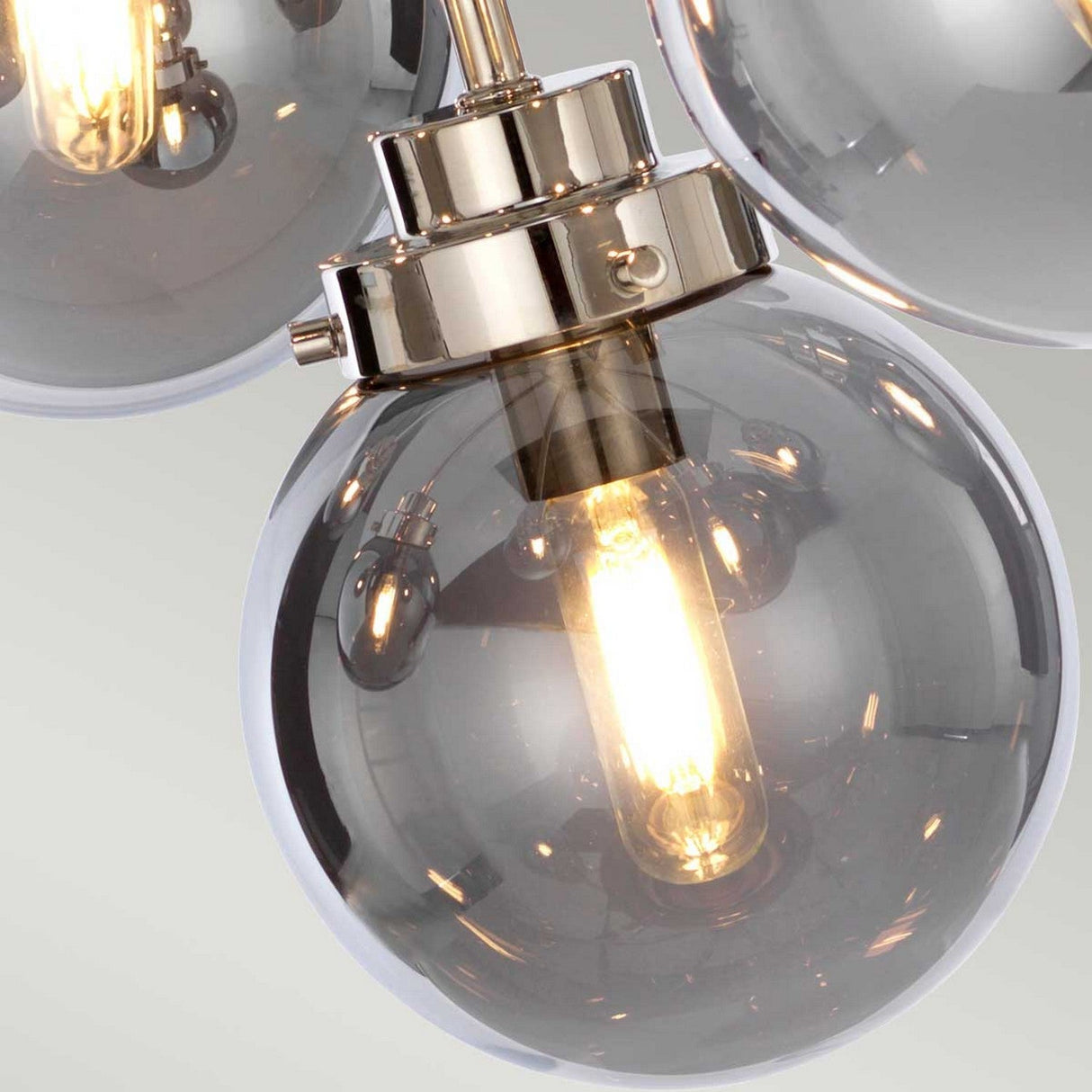 A close-up of the mid-century modern Kula 9 Light Chandelier - Polished Nickel features round glass bulbs with visible filaments. These are elegantly attached to a metallic fixture with a polished nickel finish, illuminating a warm glow against a neutral backdrop.