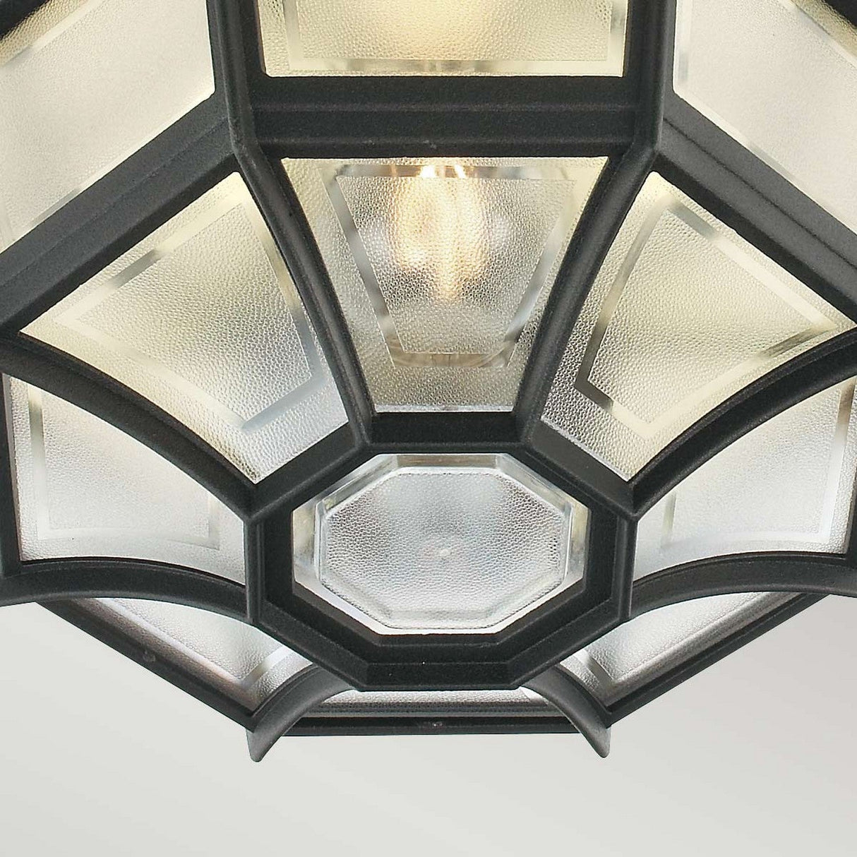 Close-up of the Latina Outdoor 1 Light Ceiling Light - Black, featuring a hexagonal design with black powder coating and frosted glass panels, allowing the bulbs to be seen inside. The geometric pattern offers a modern aesthetic, and its IP44 rating guarantees resilience in outdoor conditions.
