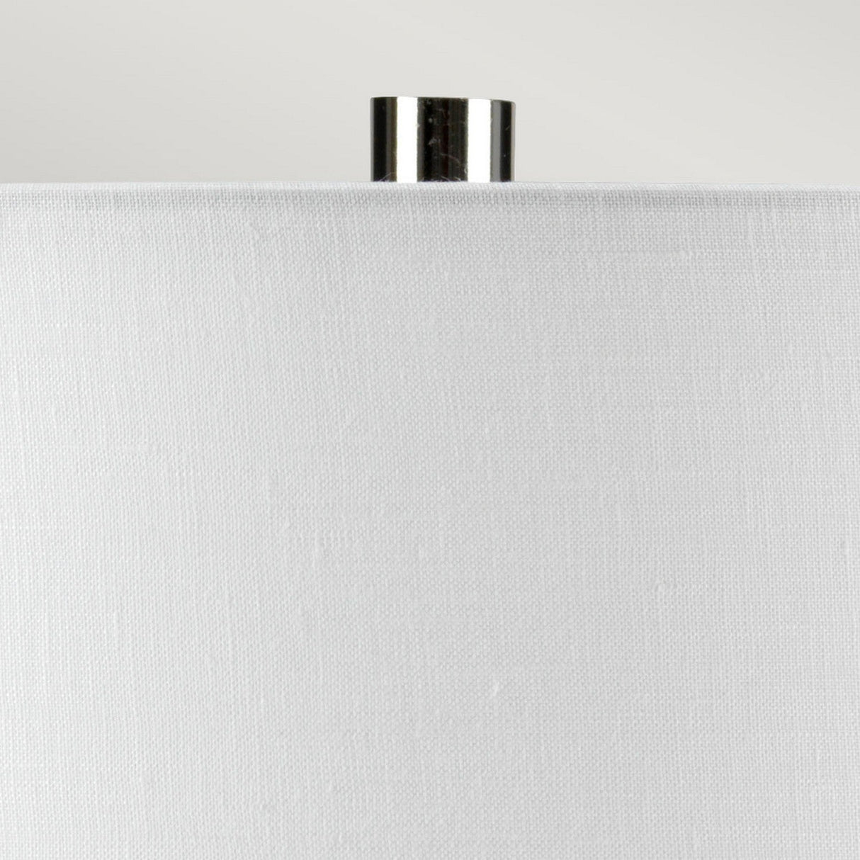 Close-up of the top portion of a white fabric lampshade with a small shiny metallic finial on top, enhancing the sleek design of the Laguna 1 Light Small Table Lamp in Turquoise & Graphite Glaze, set against a plain light gray background.