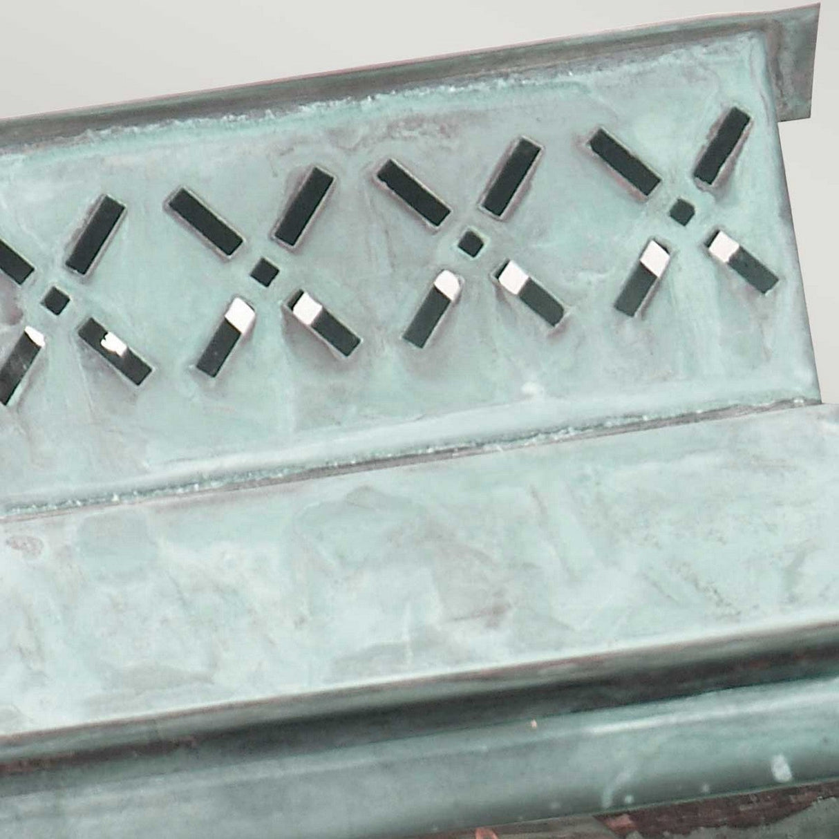 A close-up view reveals a weathered green metal bench with a backrest featuring diamond-shaped cutouts, complemented by the Lambeth Palace 1 Light Outdoor Wall Light in Verdigris. The aged seat and backrest give a rustic appearance, while the soft glow from the solid brass fixture adds charm to the scene.