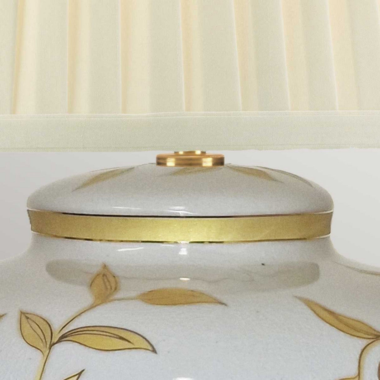 Close-up of the Leaves Brown Gold 1 Light Table Lamp, showcasing a sophisticated decorative appearance with its cream-colored, pleated fabric lampshade. The lamp base is styled to resemble Chinese porcelain, adorned with gold leaf patterns and elegant gold trim.