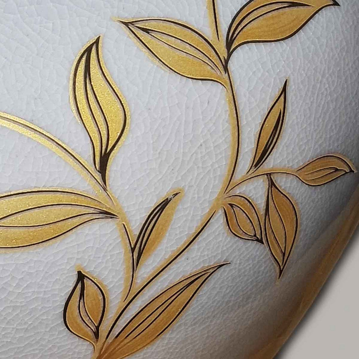A detailed view of the Leaves Brown Gold 1 Light Table Lamp - Brown & Gold showcases golden leaves and stems finely crafted on a textured white background, reminiscent of Chinese porcelain. The hand-painted design radiates an elegant and artistic vibe.