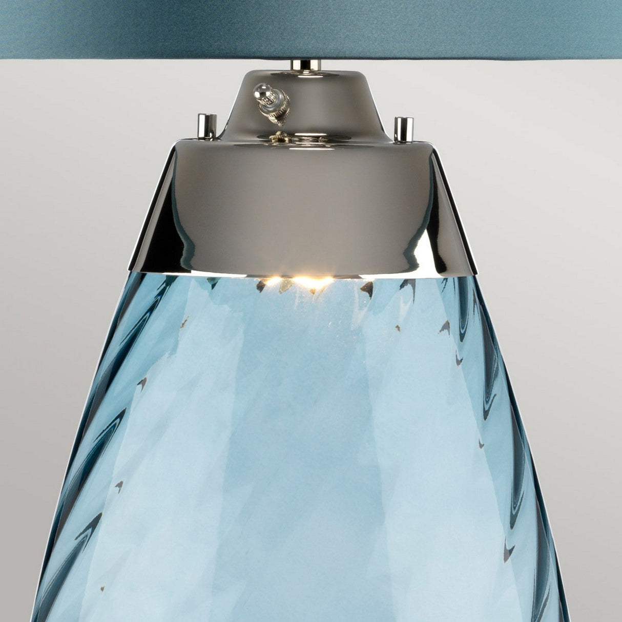 Close-up of the Lena 2 Light Large Blue Table Lamp featuring a handcrafted textured glass base in Duck Egg Blue and equipped with a 3-way switch. It is topped with a chrome fixture, complemented by a small knob above the bulb. Its elegant design stands out against the plain backdrop.