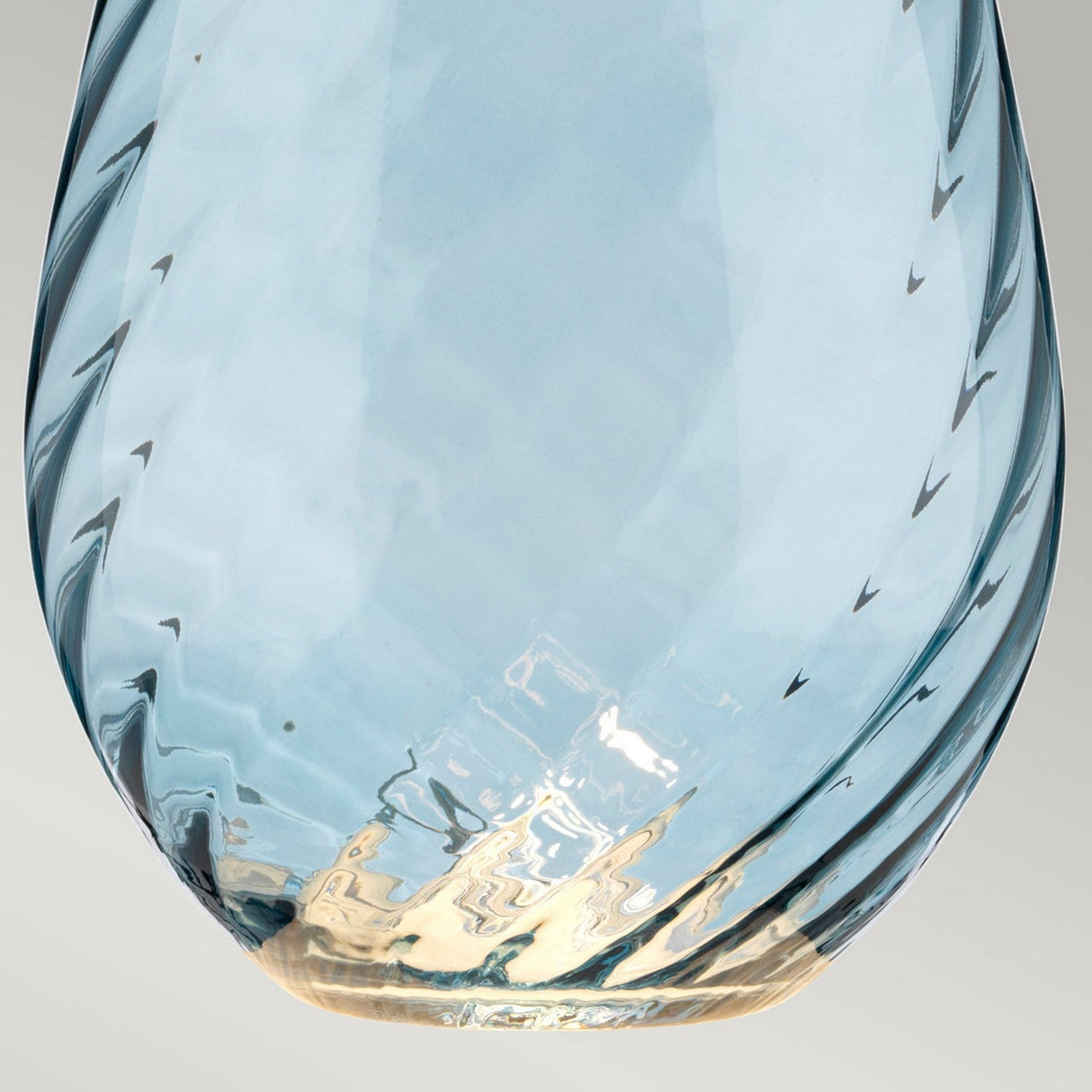Close-up of the Lena 2 Light Large Blue Table Lamp, featuring a translucent, handcrafted UK glass base with a light blue tint and twisted design. The bottom reflects light, creating a gradient from clear to faint amber. The plain and neutral background highlights its elegance, complemented by the duck egg blue shade.
