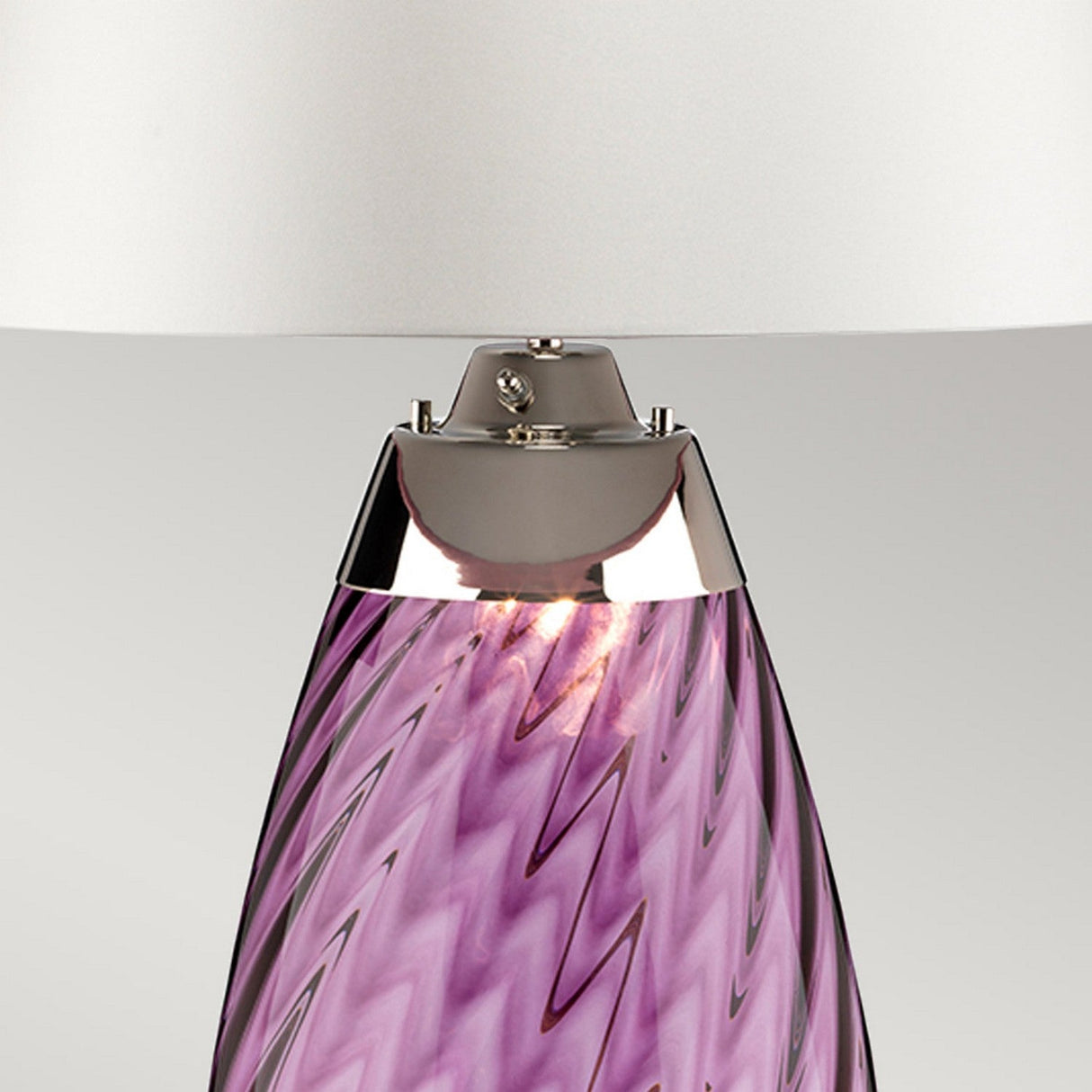 The Lena 2 Light Large Plum Table Lamp features an off-white shade and a glass base adorned with a plum zigzag pattern, crafted from mouth-blown glass and finished with a silver metallic accent. When lit, this lamp casts a warm glow that brings elegance to any room.