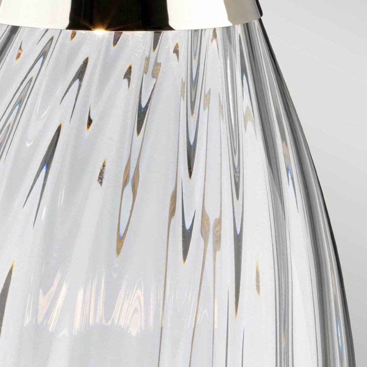 Close-up of the Lena 2 Light Small Smoke Table Lamp with a chrome top, showcasing a textured pattern of swirling lines on its smoke-tinted glass surface. The clear glass allows light to create dynamic reflections and refractions against a plain, light background.