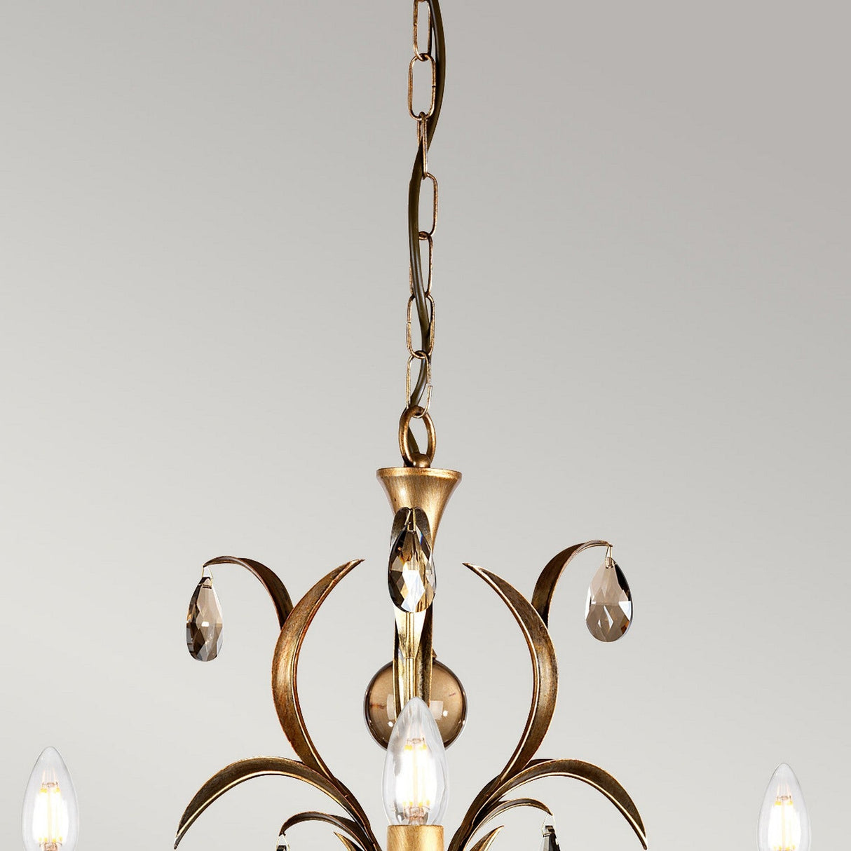Close-up of the Lily 3 Light Chandelier - Bronze Patina, featuring golden branches with a hand-patinated bronze finish and teardrop-shaped smoked cut glass droplets. Candle-like bulb holders hang gracefully from a chain against a light gray background, adding timeless elegance.