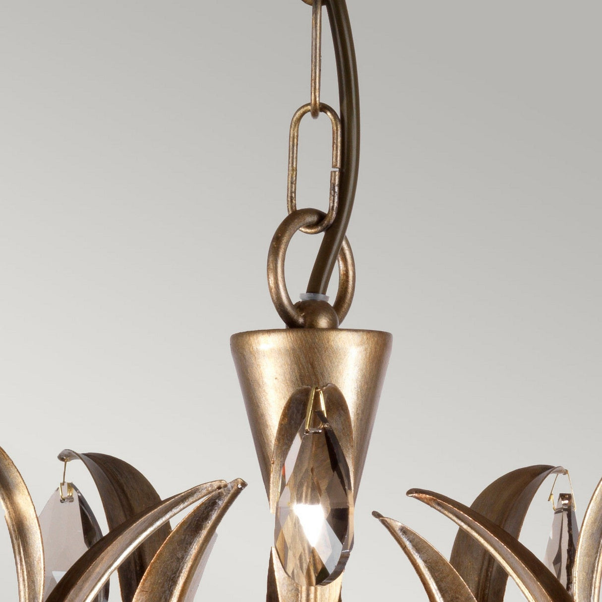A close-up of the Lily 5 Light Chandelier - Bronze Patina highlights its elegant design, featuring a metal chain link attachment in a bronze finish. This sophisticated fixture, accented with ornate golden details and adorned with smoked cut glass droplets, exudes luxury and timeless charm.