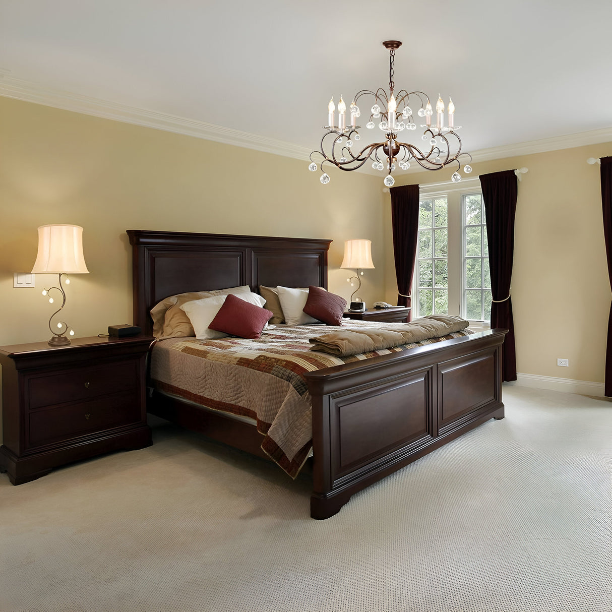 A cozy bedroom showcases a large wooden bed adorned with patterned bedding and red pillows. Two matching nightstands with modern lamps are positioned on either side of the bed, while the Lily 8 Light Chandelier - Bronze Patina hangs elegantly from the ceiling, beautifully complementing the dark curtain-covered windows.