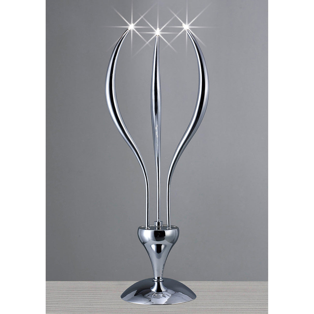 The Llamas 3 Light Table Lamp - Polished Chrome has three curved arms with sparkling lights, adding a modern sculptural touch and shining elegantly against a simple gray backdrop.