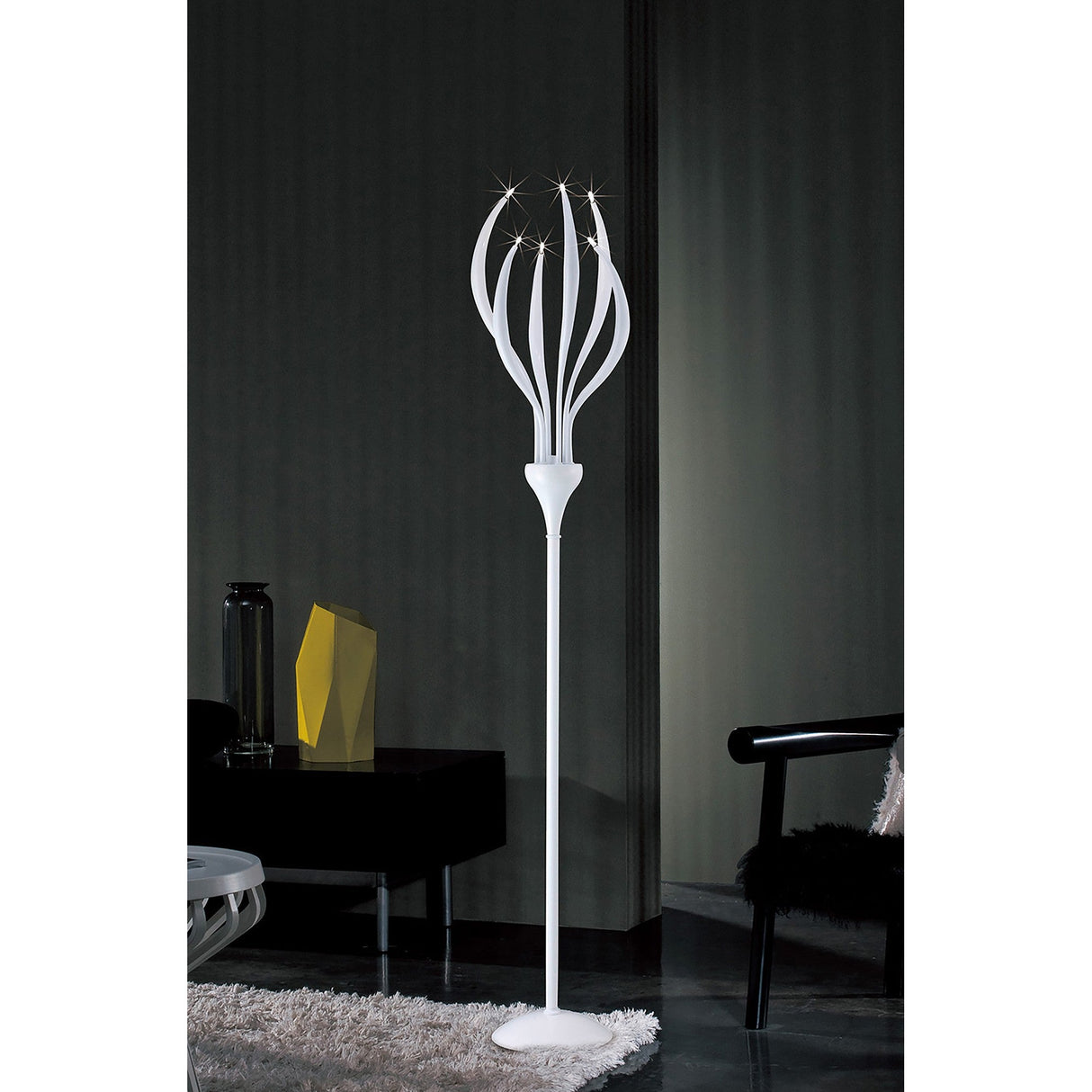 The Llamas 6 Light Floor Lamp in gloss white features curved, petal-like arms with lights at their tips, creating sculptural lighting in a dark, minimalist room with stylish furniture and decor.