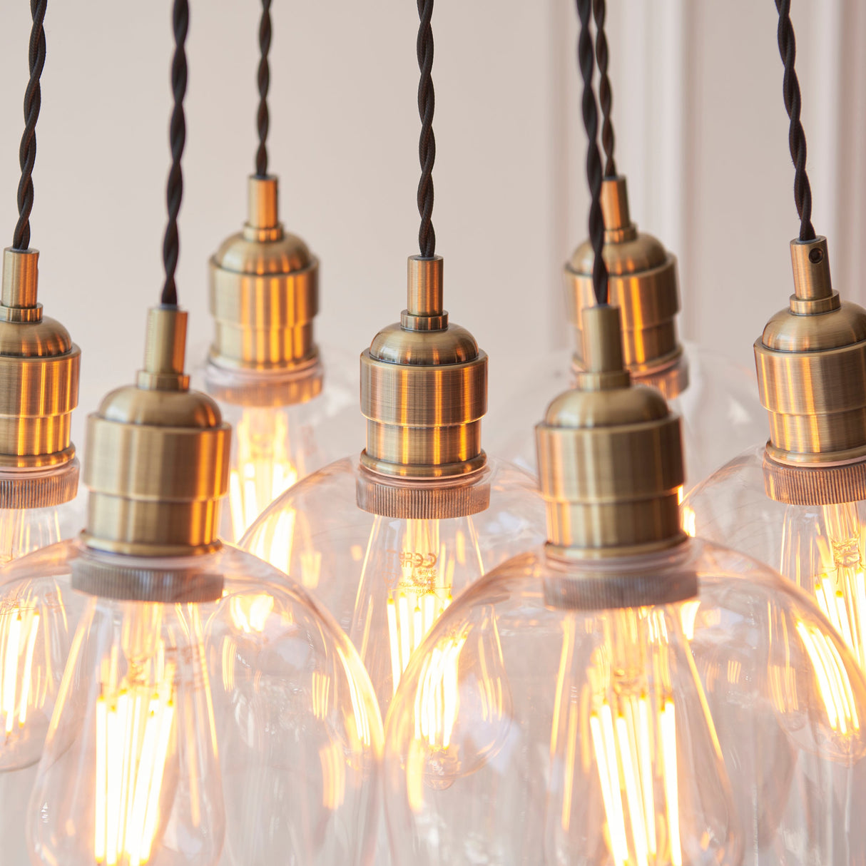 Close-up of the Lighting No.1 Quilbrook Cluster 7 Light Pendant in antique brass, showing lamp holders and clear glass globes with lit filament bulbs.