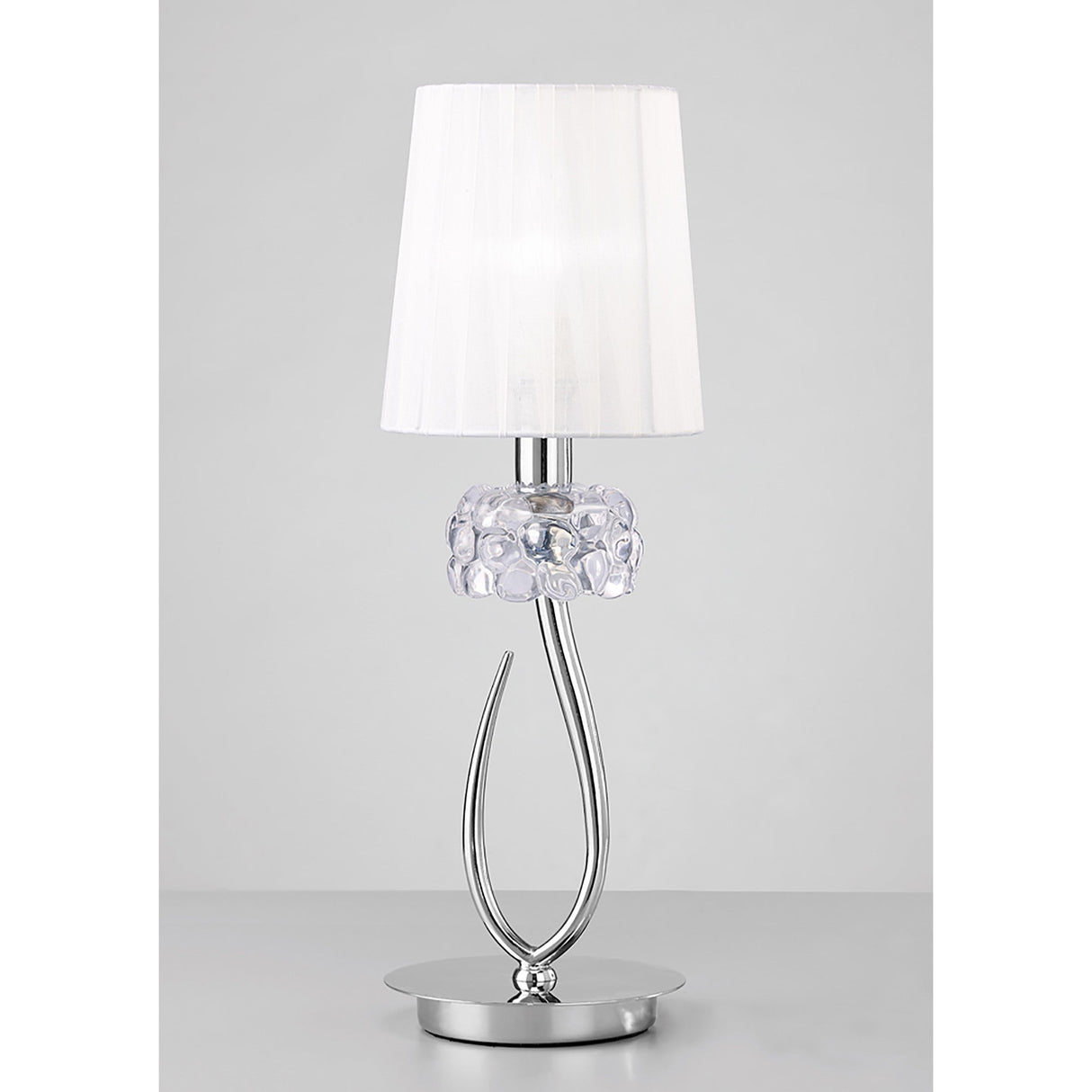 The Loewe Small 1 Light Table Lamp features a polished chrome finish, a white shade, and a decorative glass accent, inspired by modern design and displayed on a plain light gray surface.