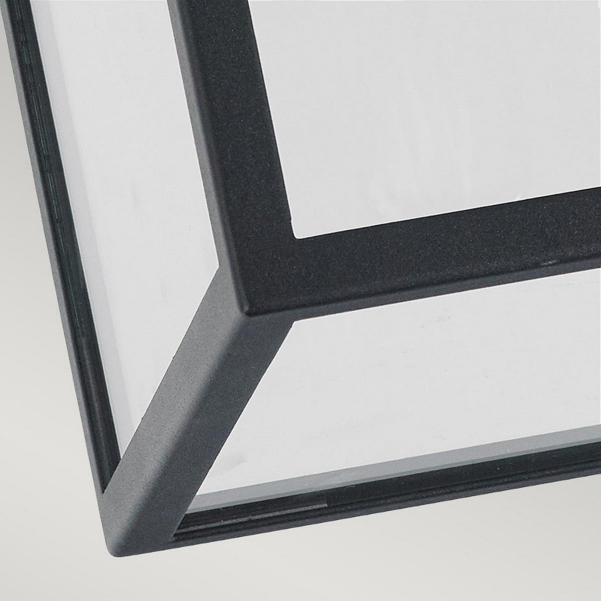Featuring the Lofoten Outdoor 1 Light Flush in black, this close-up highlights its minimalist metal and glass frame with sharp angles and clean lines against a light gray background. This fixture presents a modern, geometric design ideal for outdoor lighting, equipped with an IP44 rating to ensure weather resistance.