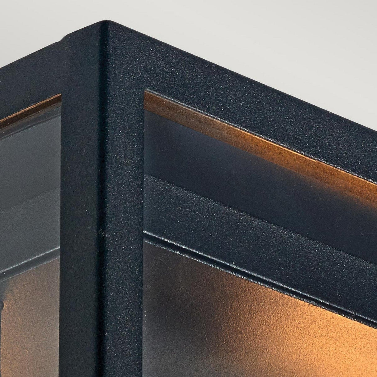 Close-up of the corner of the Lofoten Outdoor 2 Light Flush in black, showcasing its modern, rectangular design. The sharply defined edges frame a warm glow from within that casts onto a textured surface, making it perfect for enhancing sophisticated outdoor lighting.