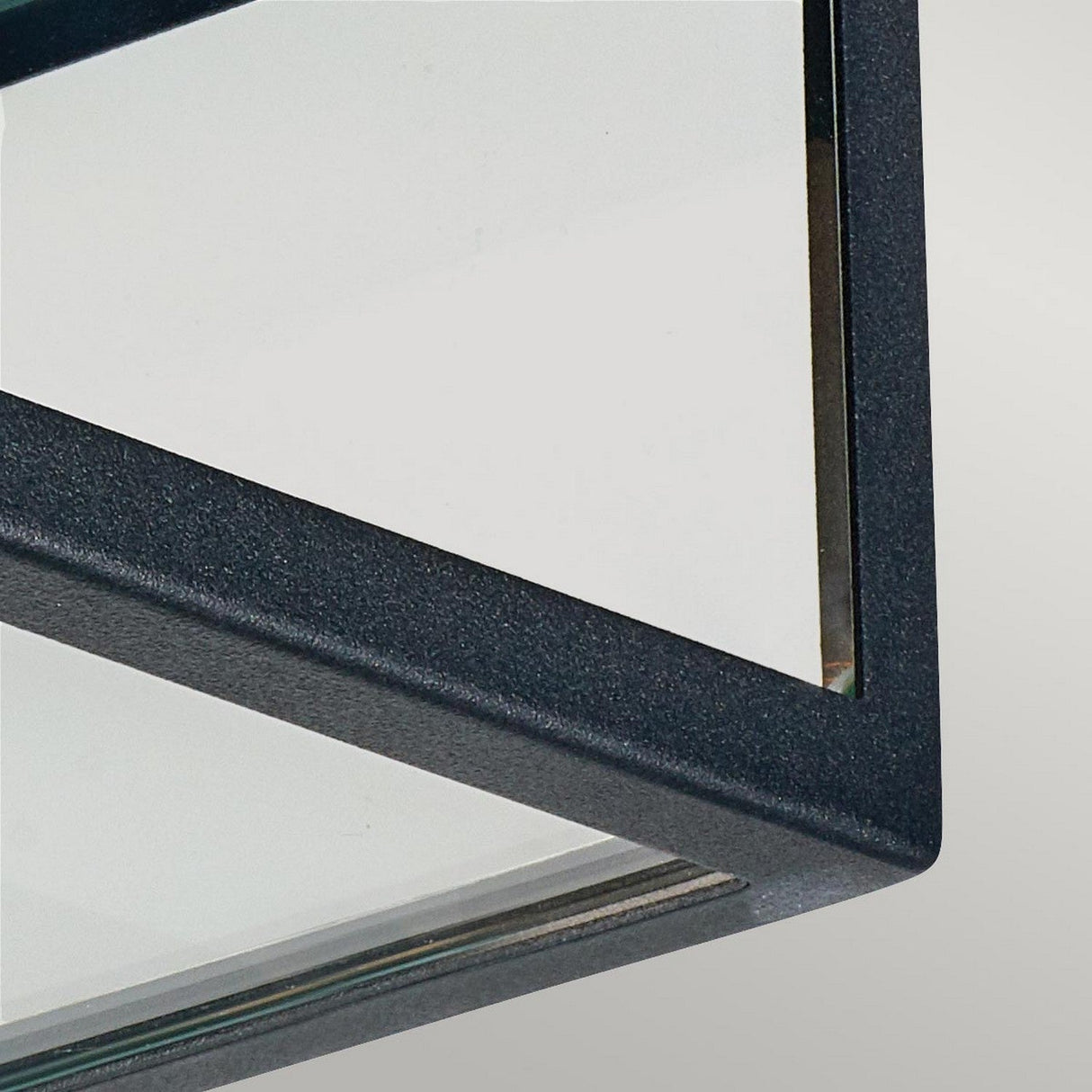 Close-up of the corner of the Lofoten Outdoor 2 Light Flush in a black metal frame. The minimalist design highlights the contrast between its transparent glass and dark frame, evoking a modern outdoor fixture set against a light gray background.