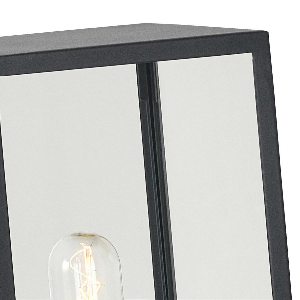 A detailed view of the Lofoten 1 Light Pillar - Black reveals an electro-galvanized steel frame with a glass panel, highlighting a vintage-style filament light bulb. This outdoor lighting fixture exemplifies modern industrial design with its clean lines and minimalist aesthetic, making it ideal for contemporary spaces.