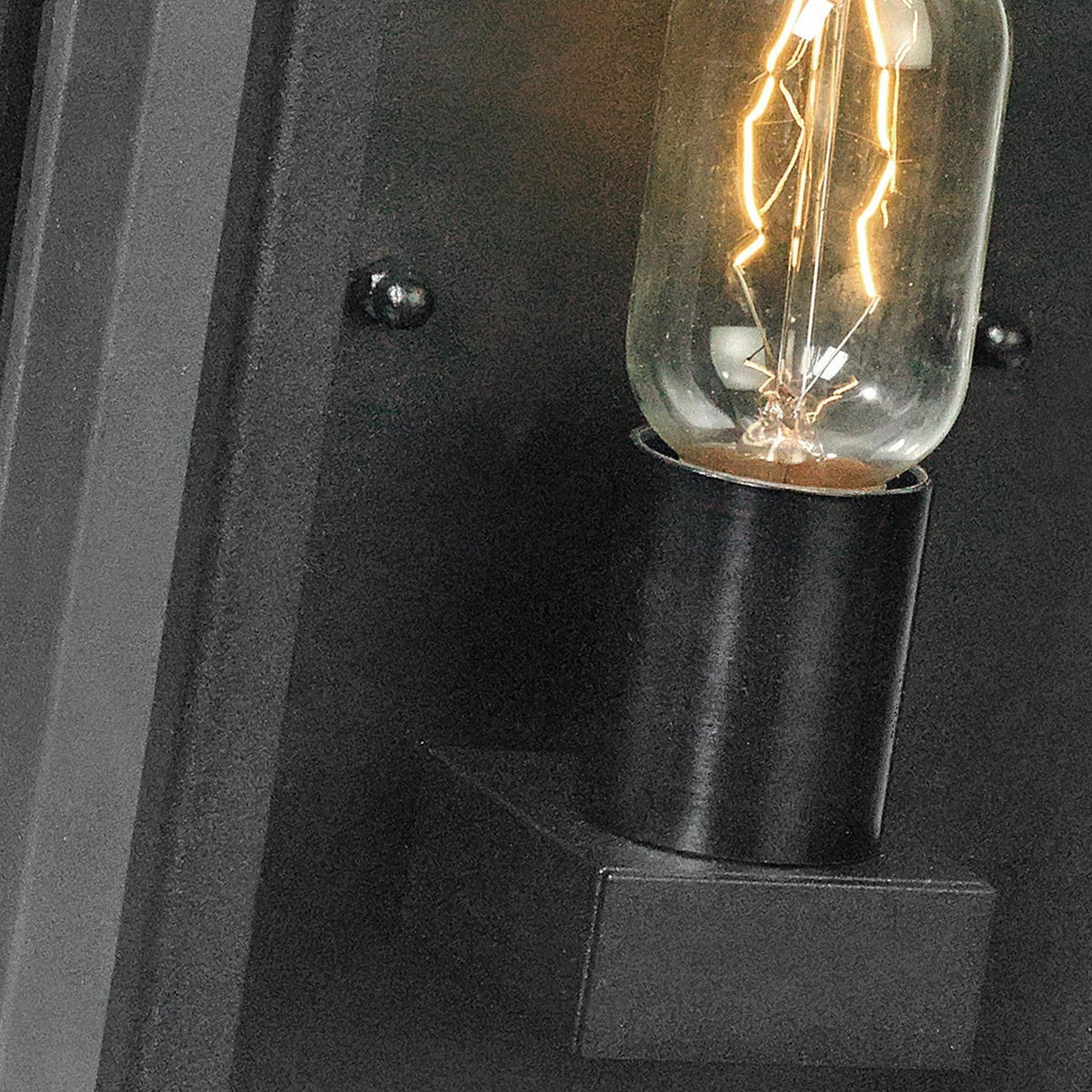 A close-up of the Lofoten Outdoor 1 Light Half Lantern in black showcases a vintage-style Edison bulb with a visible filament. Ideal for outdoor lighting, this elegant fixture emits a warm glow that highlights the intricate design of the filament inside the glass and features an IP44 rating for enhanced durability.