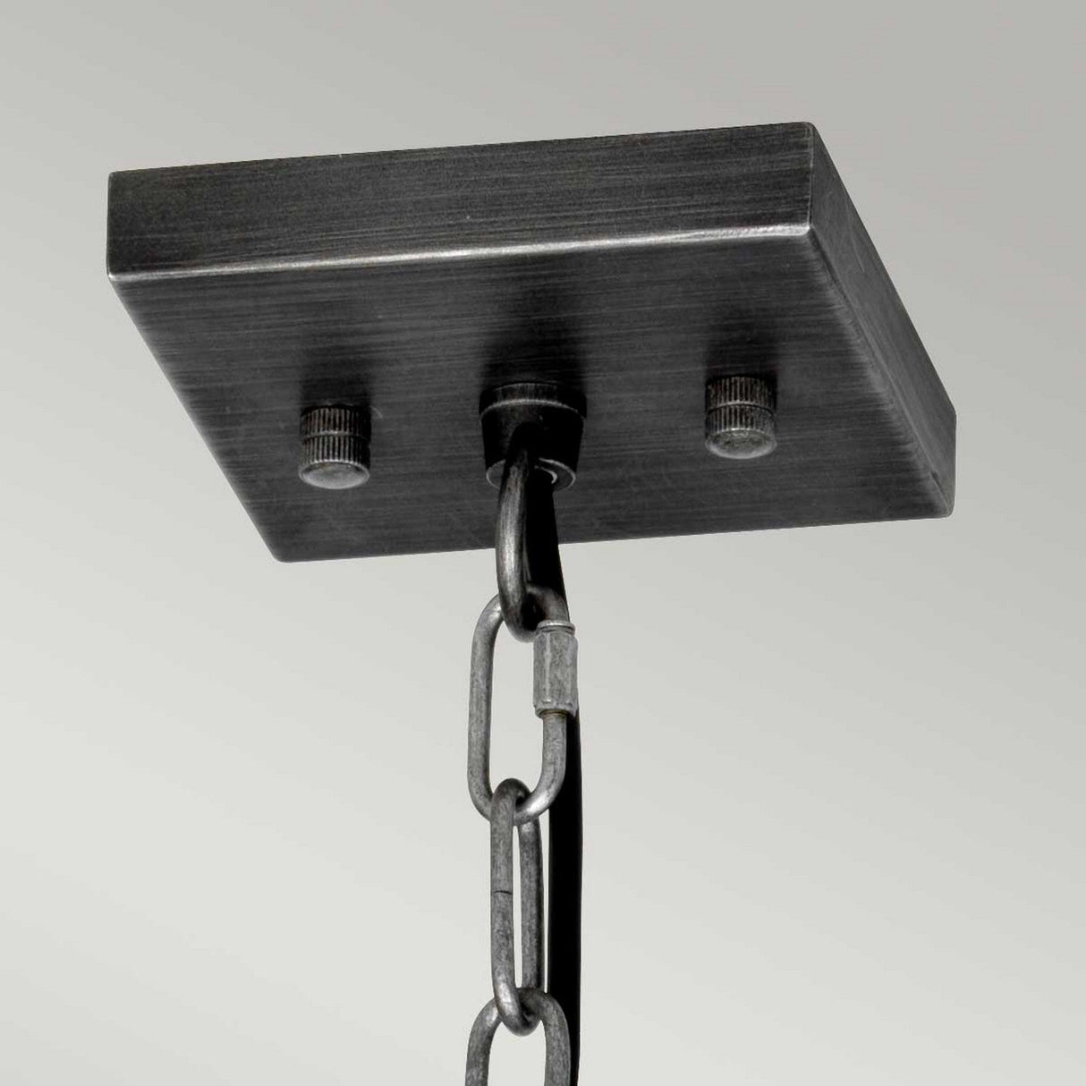 Close-up of a graphite metal ceiling mount with two screws, from which a metal chain is suspended. The chain supports an unseen object below, exuding vintage charm. The mount and chain have a brushed, industrial design reminiscent of a classic Louvre 1 Light Pendant.