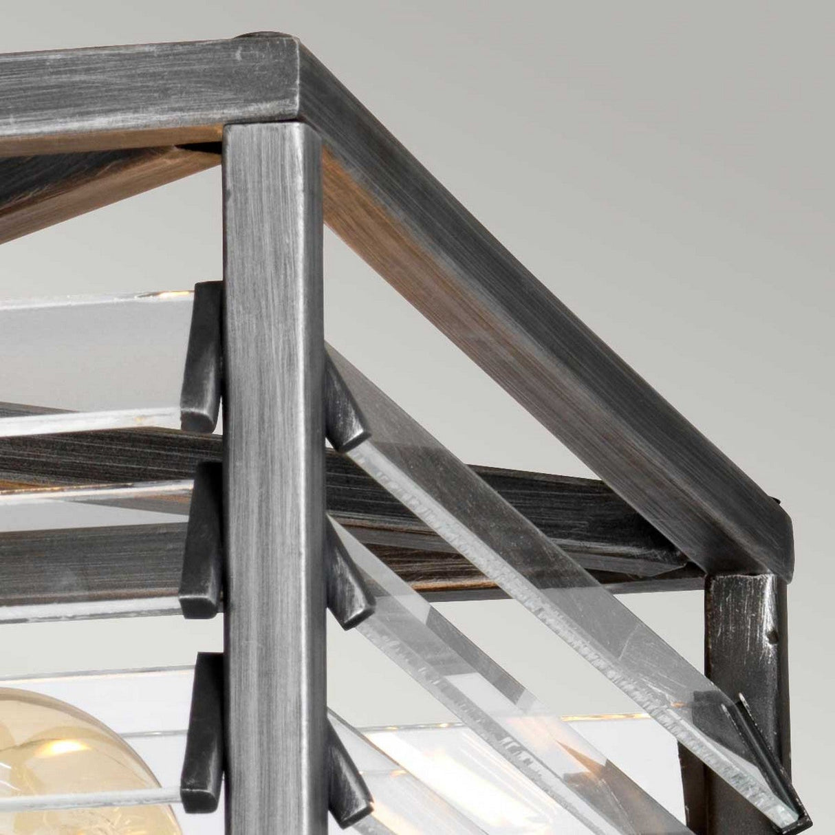 Close-up of the Louvre 4 Light Flush - Graphite, showcasing a geometric metal frame with clear glass panels and a graphite finish. Its angular, flush design highlights industrial lighting with an exposed light bulb beneath.