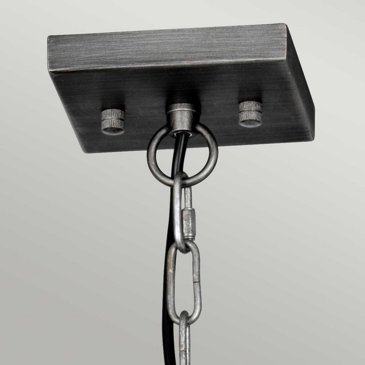 The Louvre 6 Light Chandelier in graphite features a close-up view of its rectangular metal ceiling bracket, complete with attached chain and wire, perfect for suspending industrial chandelier fixtures. With two visible screws and chain links that connect to a loop securing the wire, it exudes vintage charm.
