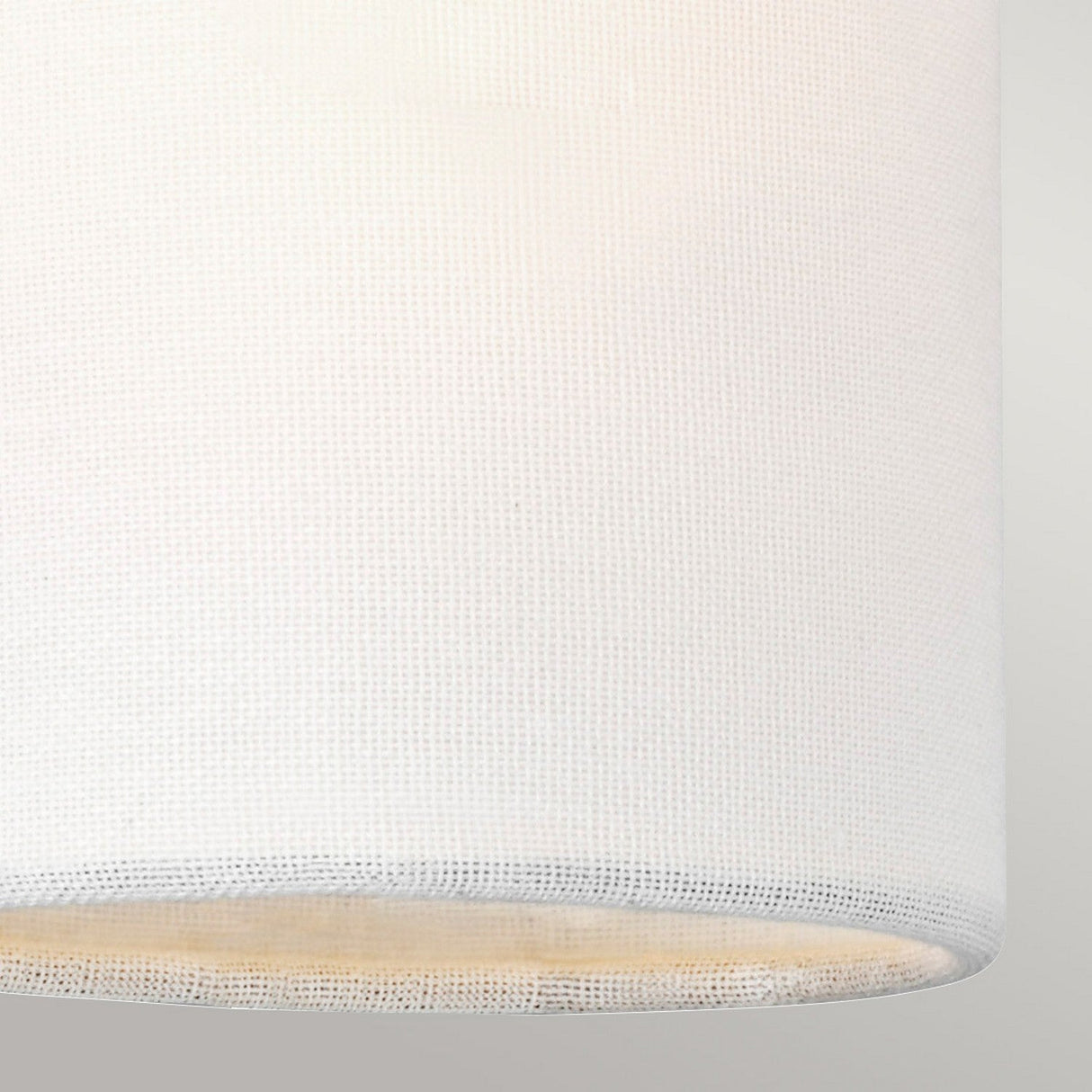 Close-up of a Clip Shades - Ivory Linen cylindrical lampshade against a neutral background. The woven fabric, featuring its subtle grid pattern, is enhanced by ambient lighting, beautifully highlighting the material's texture.