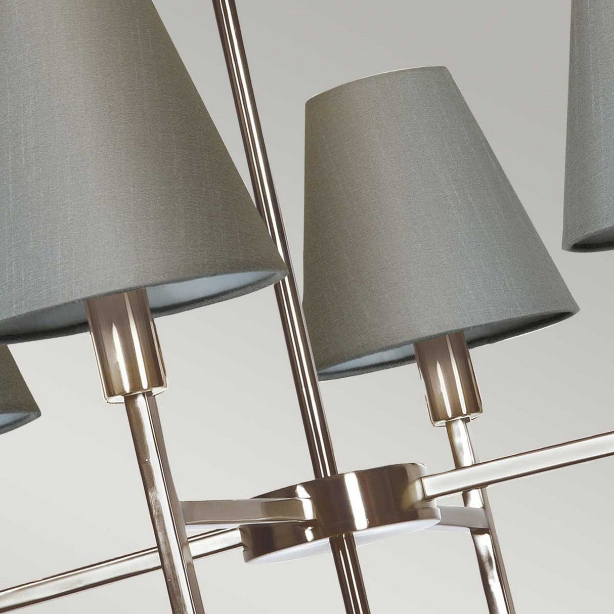 A close-up view of the Lucerne 4 Light Chandelier - Brushed Nickel With Grey Shade reveals multiple gray fabric lampshades and sleek brushed nickel fixtures. Its design showcases intersecting metallic rods that support the lampshades, offering an elegant and modern luxury appeal.