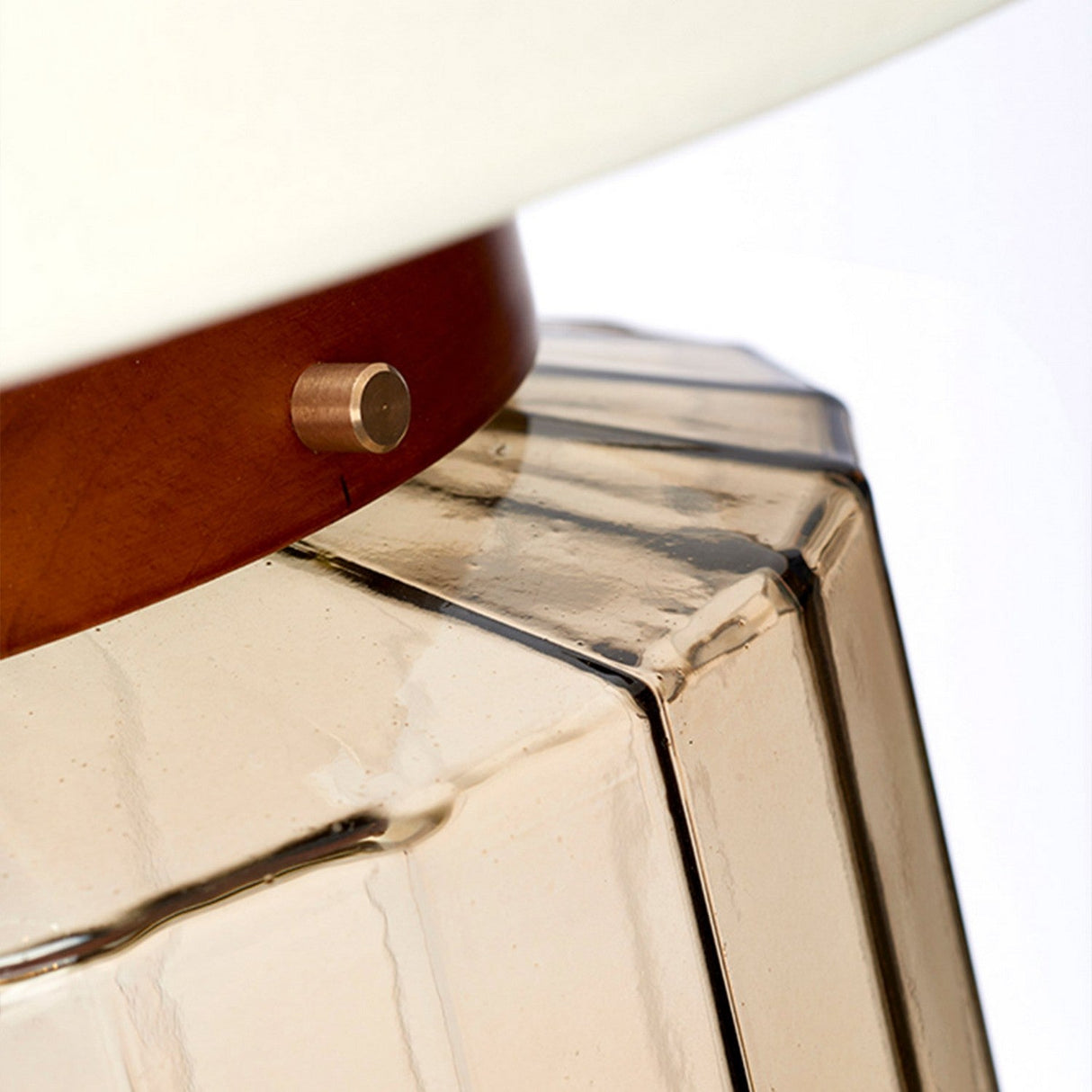 Close-up of the Luga Table Lamp, showcasing its modern design with a geometric faceted base crafted from recycled amber-toned glass and accented by aged brass elements alongside wooden details, giving it an elegant and contemporary appearance.
