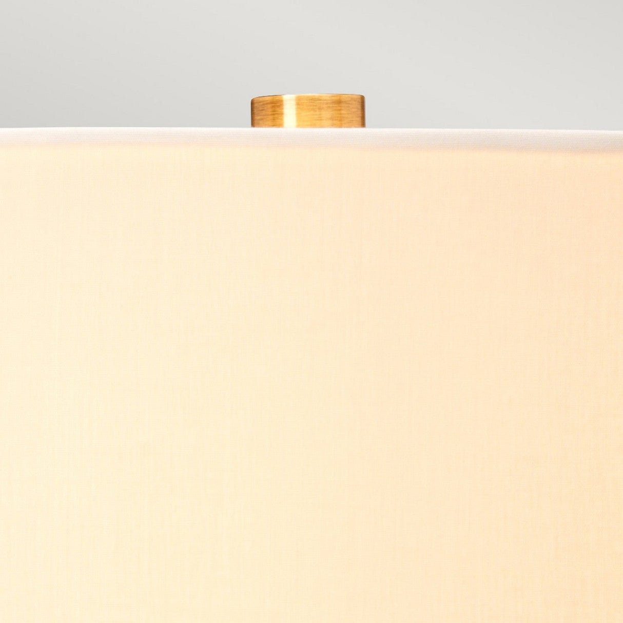 Close-up of a beige lampshade against a light gray background. Visible above its recycled glass base, the top of the Luga Table Lamp - Aged Brass showcases elegant aged brass detailing, highlighting its eco-conscious design.