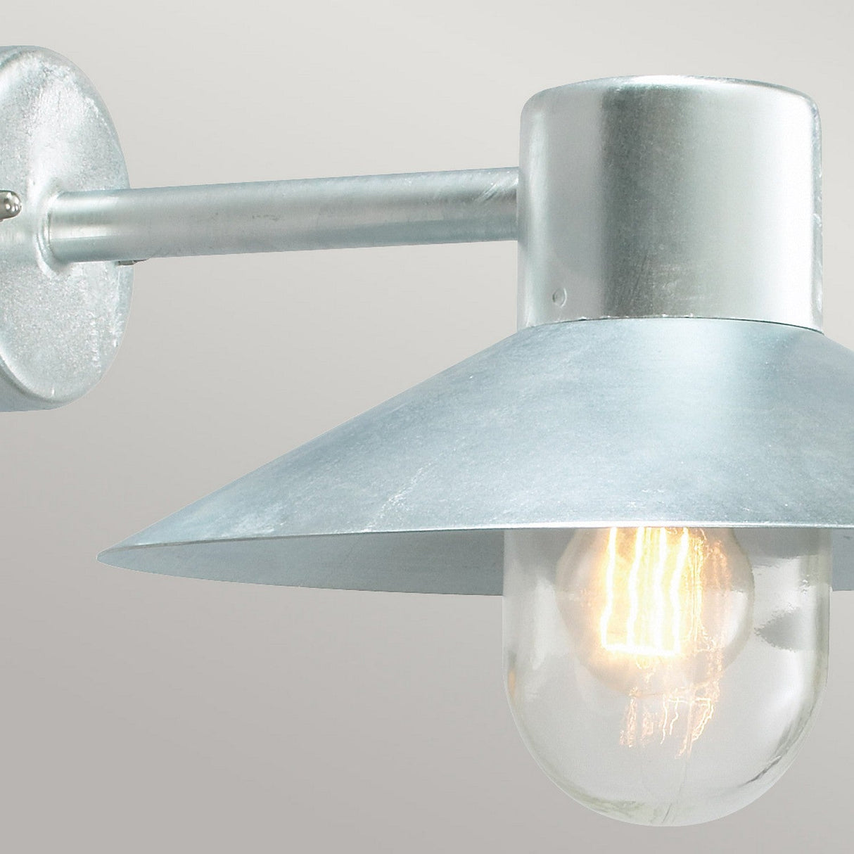 The Lund Outdoor 1 Light Wall Lantern in silver boasts a modern, industrial style crafted from galvanized steel. It features a conical shade with a metallic finish. Its IP65 rating guarantees outdoor durability, while the exposed bulb casts a warm glow that complements its sleek and elegant design.