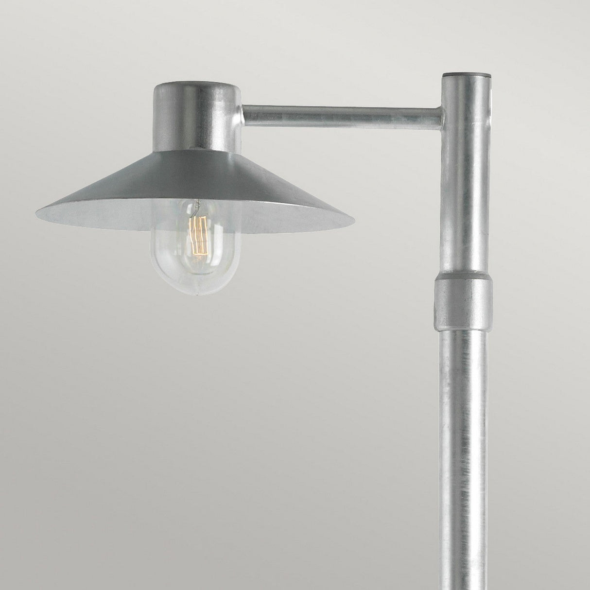 Introducing the Lund 1 Light Lamp Post in Silver, a minimalist street lamp featuring a conical shade and exposed bulb. Crafted from galvanized steel, its sleek and modern design includes an adjustable height post, seamlessly blending into any plain gray background for the perfect outdoor lighting solution.