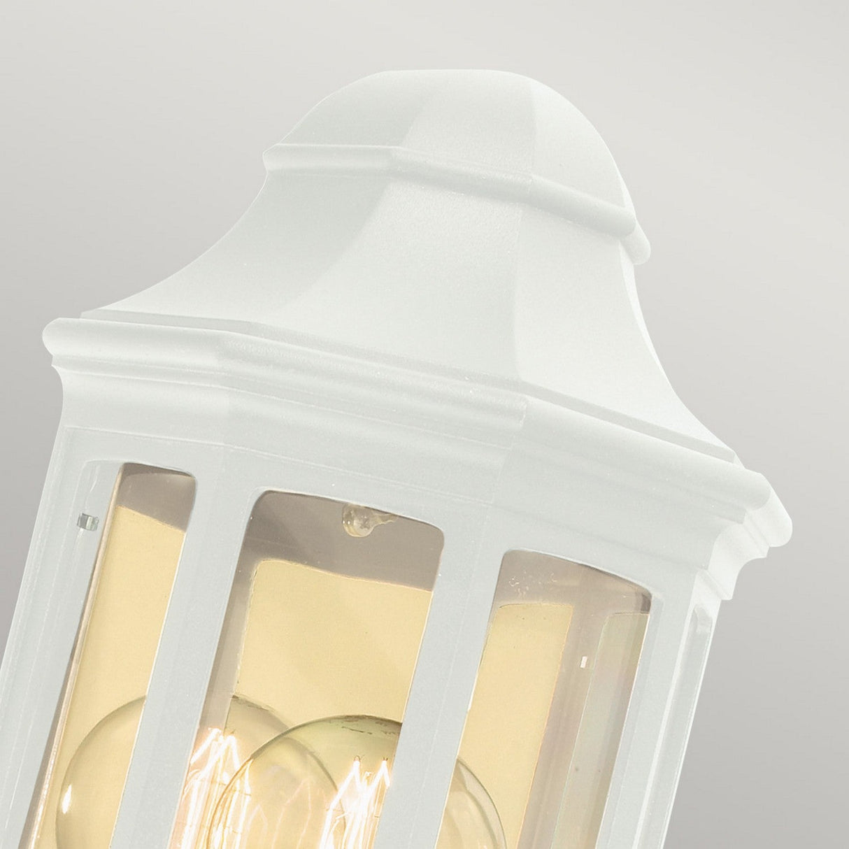 Close-up of a white Malaga Outdoor 1 Light Mini Wall Lantern, featuring a vintage-style design crafted from cast aluminum with clear glass panels, showcasing two visible light bulbs inside against a neutral gray background.