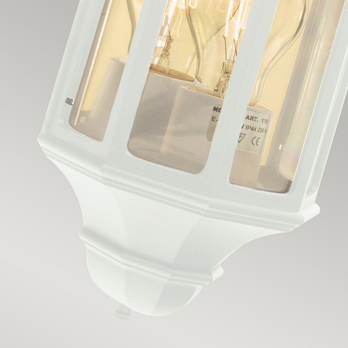 The Malaga Outdoor 1 Light Mini Wall Lantern in white is crafted from cast aluminium, featuring a clear glass enclosure that showcases an exposed light bulb against a light gray background. It has an IP54 rating and boasts a classic, angular design with a slightly tapered base.