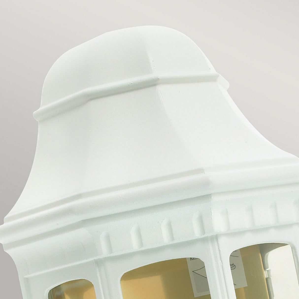 Close-up of the Malaga Outdoor 1 Light Wall Lantern in white, showcasing its vintage-style design with a curved top and clear glass panes enclosing the interior light fixtures. The soft gray background highlights the elegant and durable craftsmanship of this outdoor lighting solution.