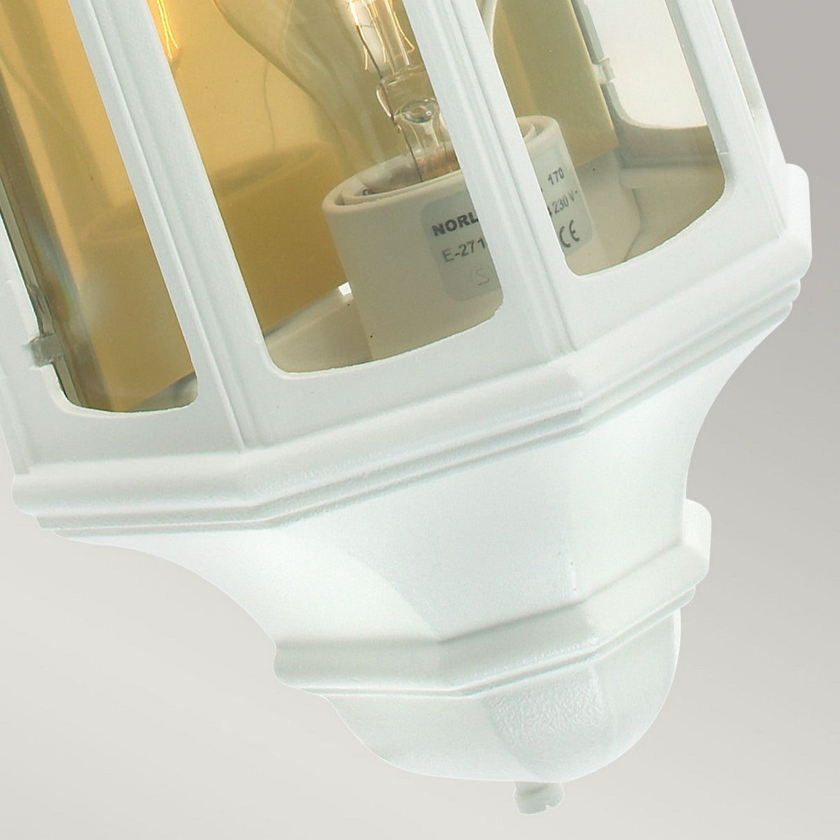 Close-up of the Malaga Outdoor 1 Light Wall Lantern in white, featuring a glass enclosure for durability and ideal for exterior lighting. The lantern showcases a classic design with a visible light bulb inside its multi-paneled casing, set against a neutral beige background.