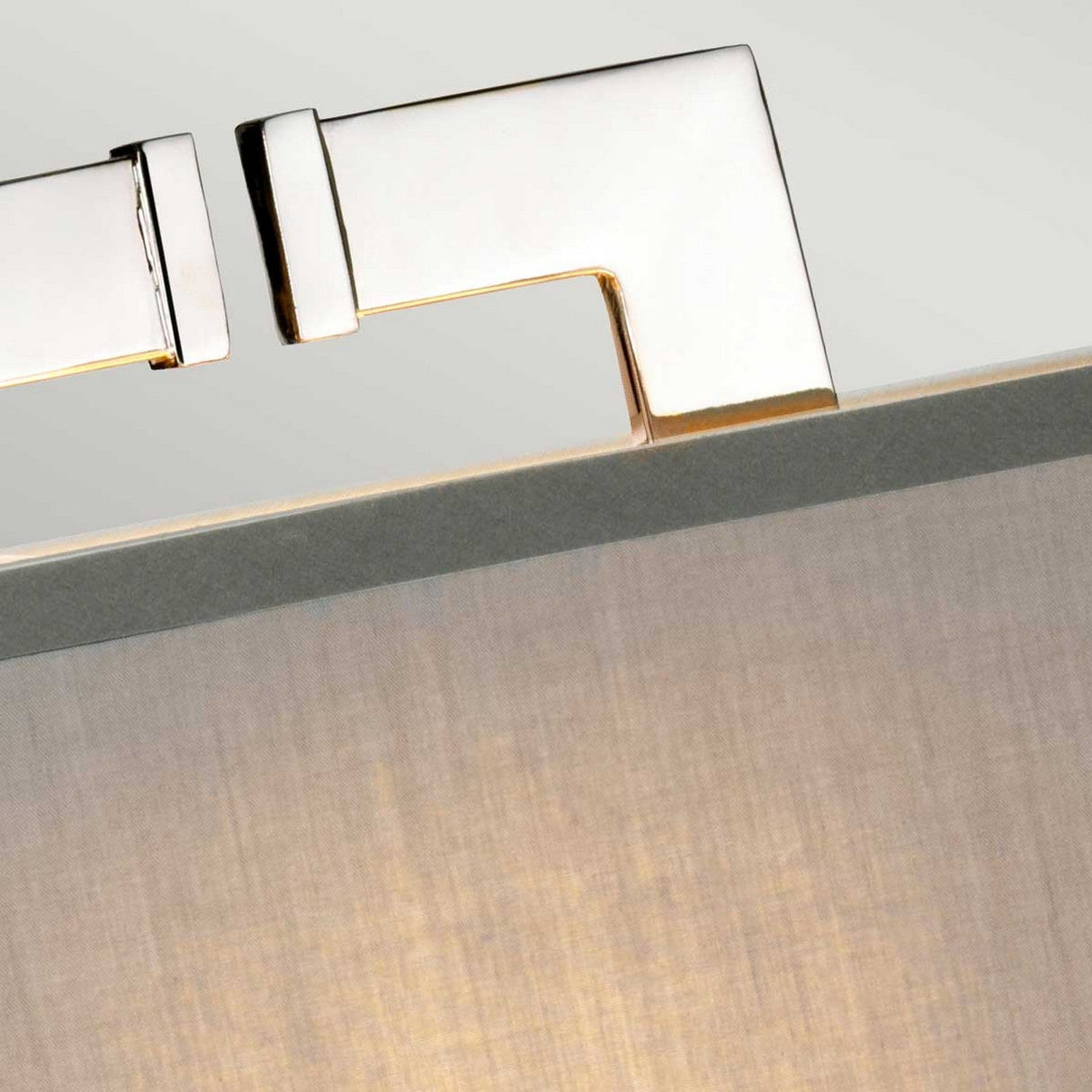 A close-up of a sleek, modern metal hinge secured to light-colored fabric evokes the polished nickel finish typical of contemporary aesthetics. The reflective hinge connects two parts at a right angle, embodying minimalist design much like the Magro 1 Light Table Lamp in Polished Nickel.