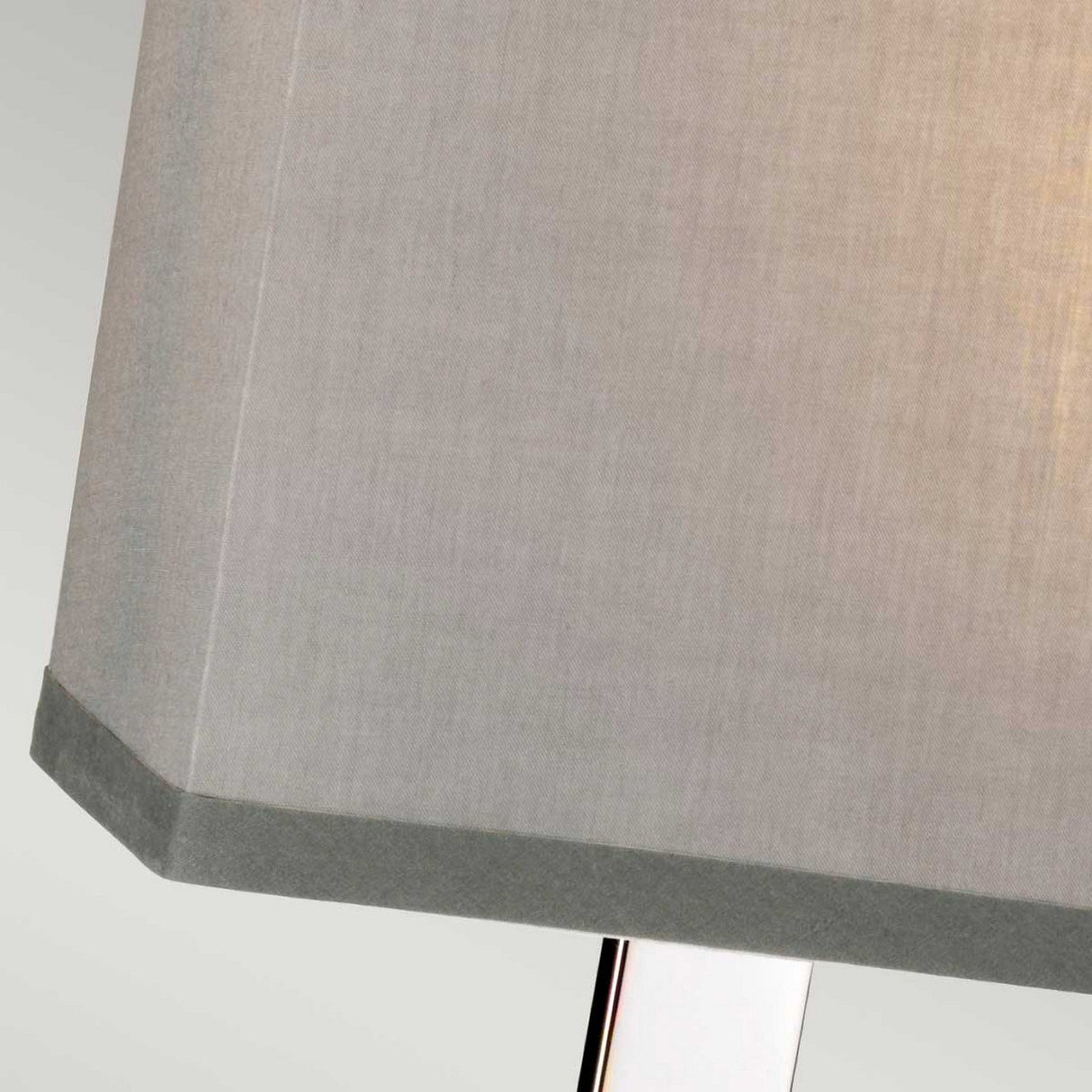 A close-up of the Magro 1 Light Table Lamp - Polished Nickel highlights its light gray fabric shade and polished nickel base against a neutral backdrop. This modern lighting fixture is illuminated, emitting a warm glow.