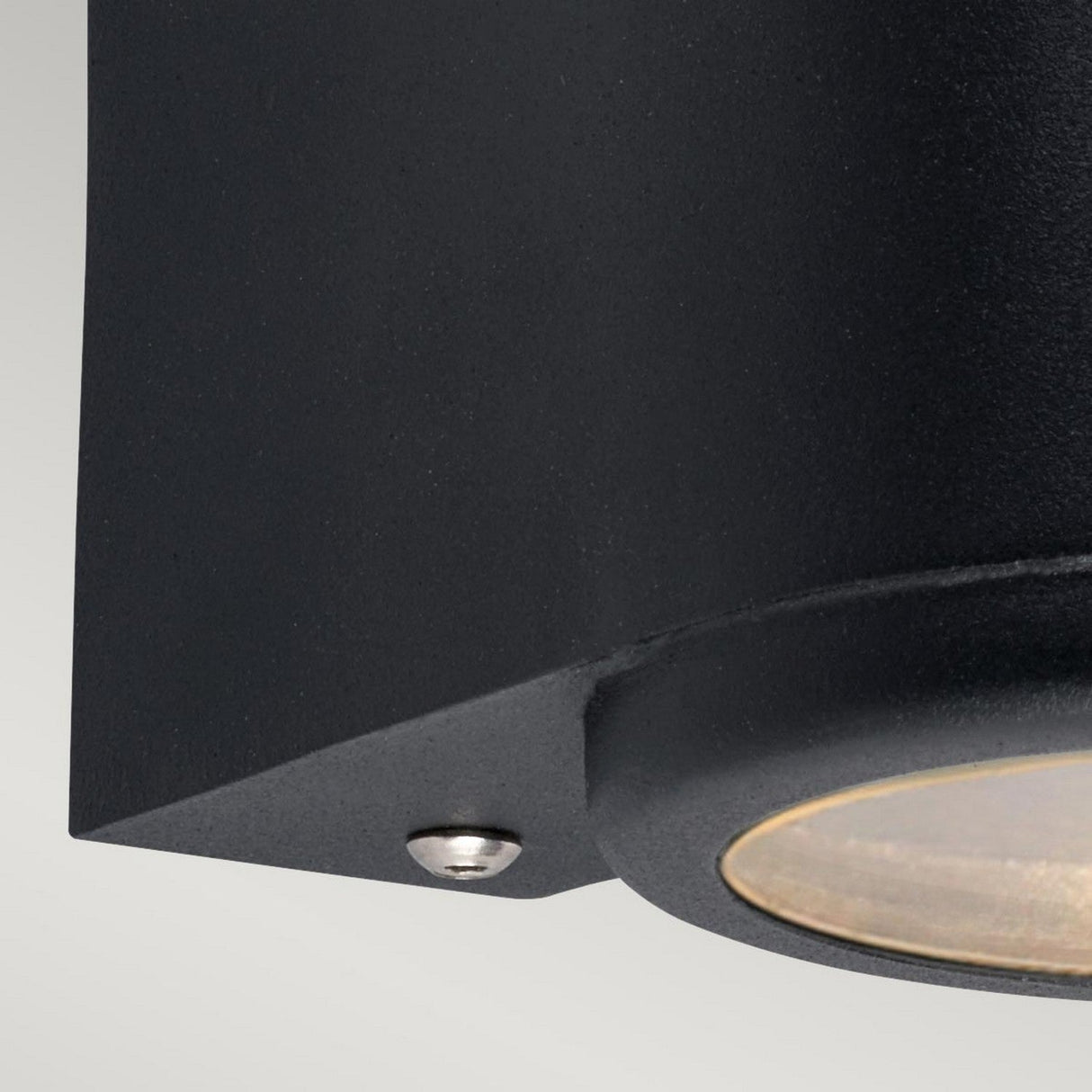 Close-up of the Mandal Outdoor LED Down Wall Light in black against a neutral background. The fixture has a cylindrical design with a visible screw and transparent cover for light emission, and it is IP44 rated for outdoor use. Its texture looks matte and sturdy.