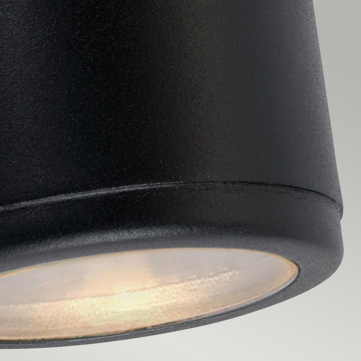 Close-up view of the Mandal Outdoor LED Down Wall Light in black, featuring a smoothly matte cylindrical design and a softly lit LED bulb. The image highlights the bottom portion of this IP44 rated fixture against a neutral background, ideal for outdoor lighting applications.