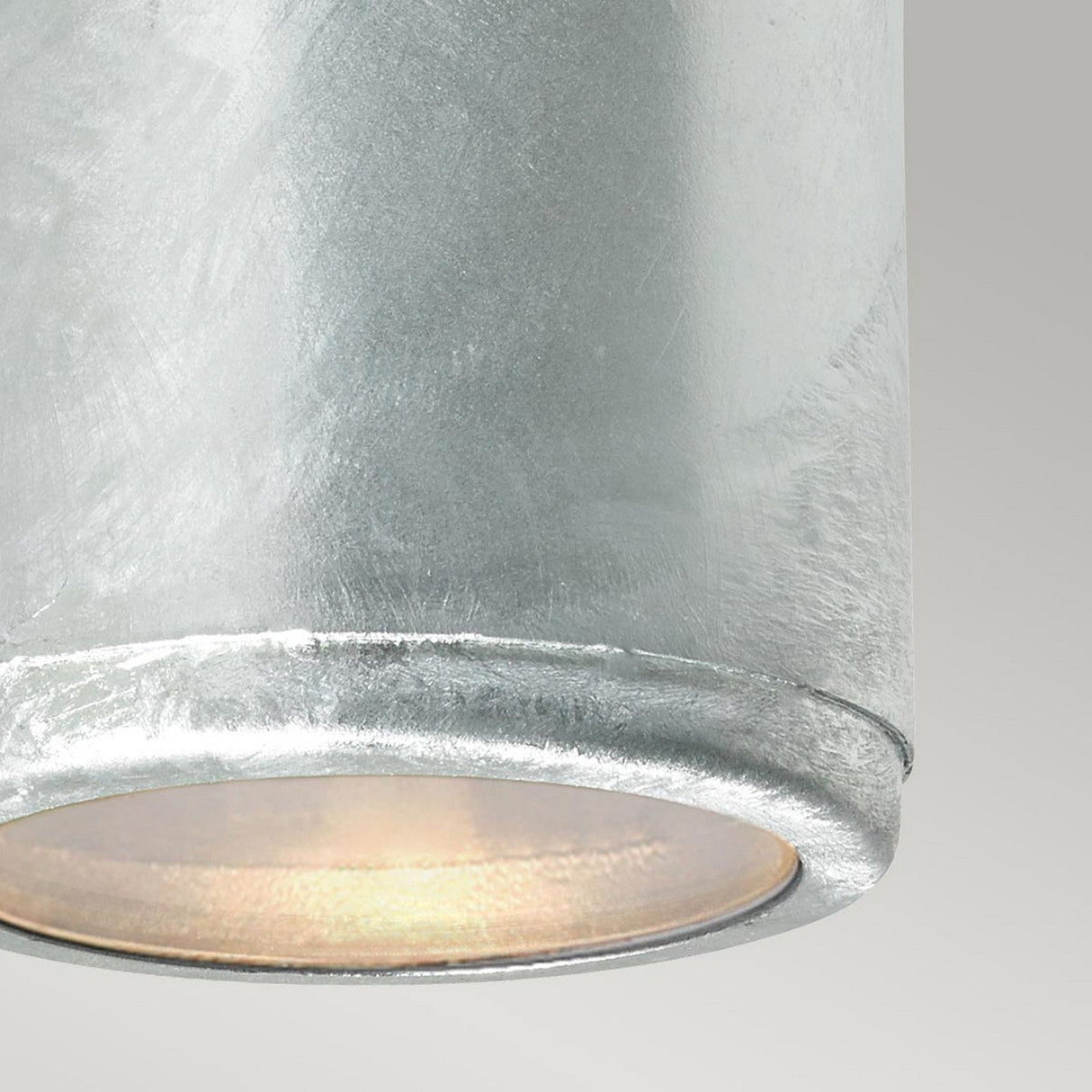 Close-up of the Mandal Outdoor LED Down Wall Light - Silver, showcasing its modern cylindrical design and textured metallic finish crafted from galvanized steel. Emitting a warm glow with energy-efficient LED technology, it stands out against a soft gray background in simple industrial elegance.