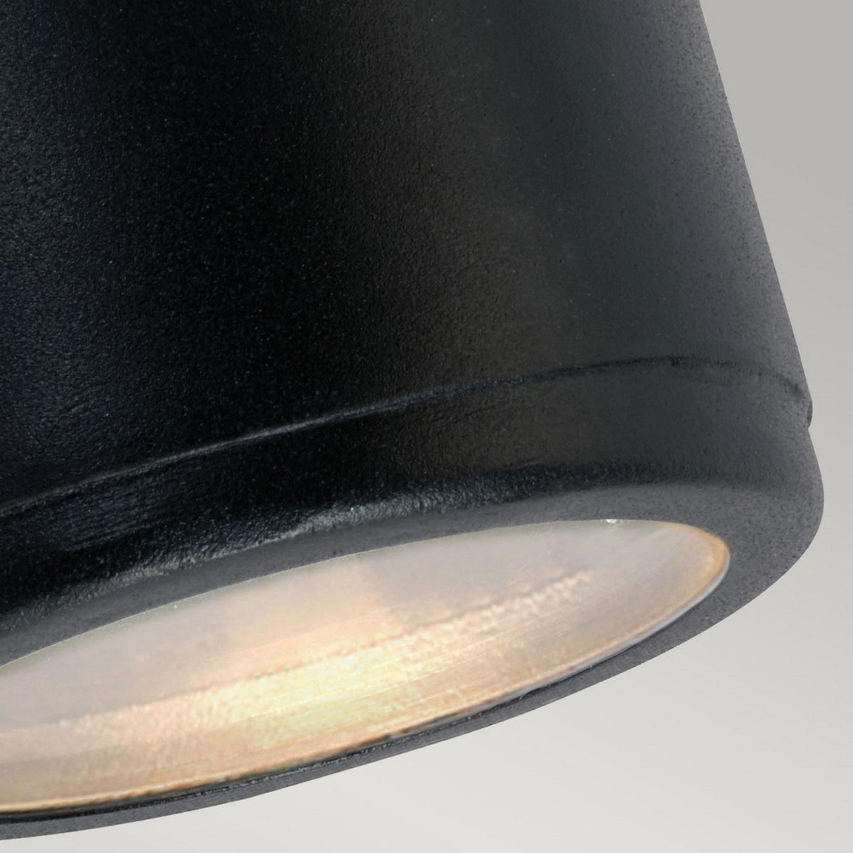 Close-up of the Mandal Outdoor LED Up/Down Wall Light in black, featuring a glowing bulb that casts a warm light against a neutral background. The sleek design harmonizes with galvanized steel accents typically seen in up/down lighting fixtures, blending contemporary elegance with timeless appeal.
