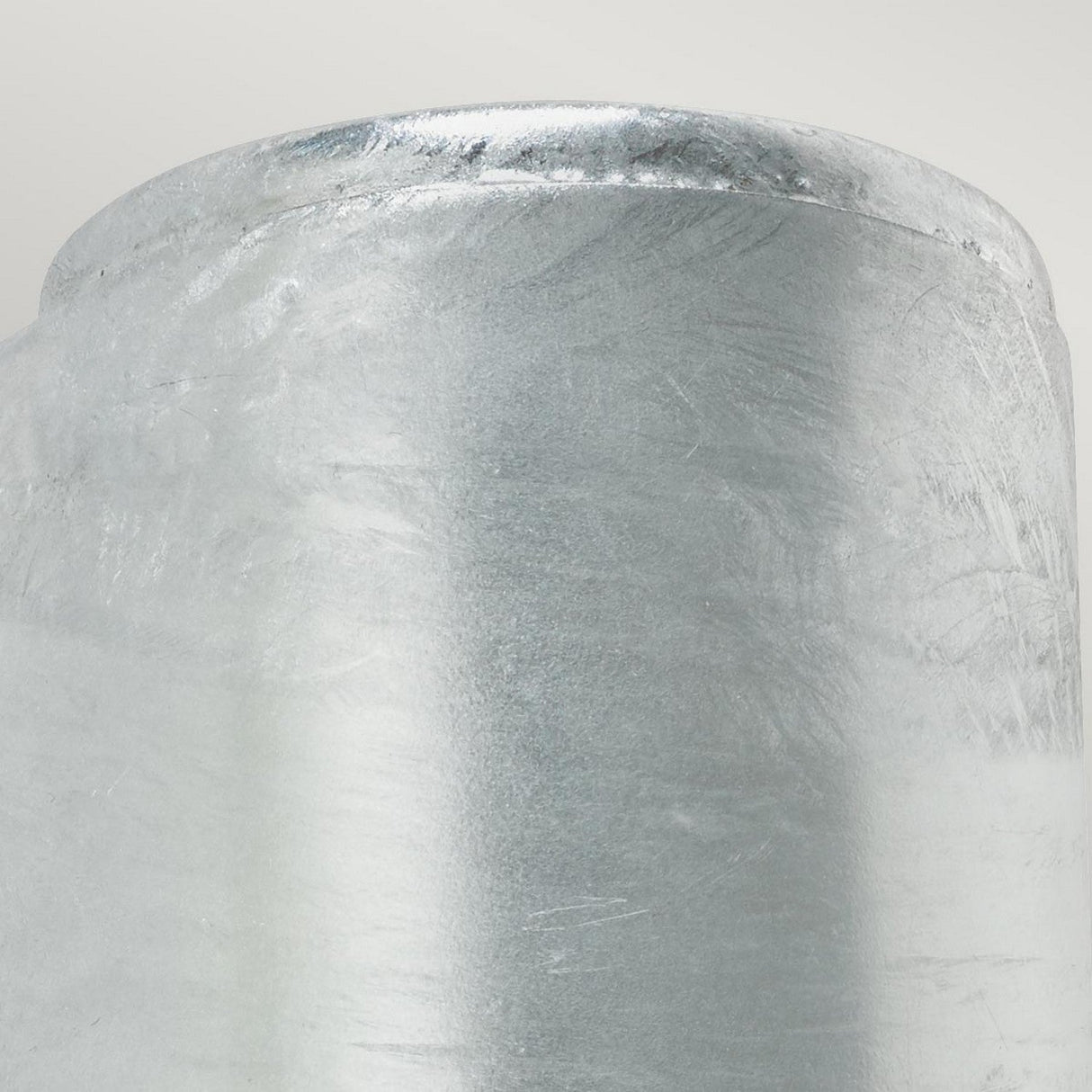 Close-up of the Mandal Outdoor LED Up/Down Wall Light crafted from durable galvanized steel, featuring a smooth and shiny, textured cylindrical design. The top edge is rounded and exhibits a brushed, silvery finish. This wall light is displayed against a soft, light gray background.