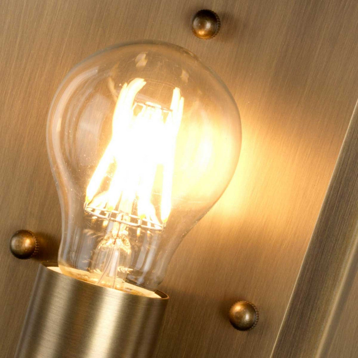 The Mansion 1 Light Outdoor Wall Light in Aged Brass exudes a warm glow against its metallic gold background, enhanced by four decorative rivets. Encased in a cylindrical holder, this handcrafted piece softly illuminates its surroundings, offering an exquisite touch to any outdoor wall light setting.