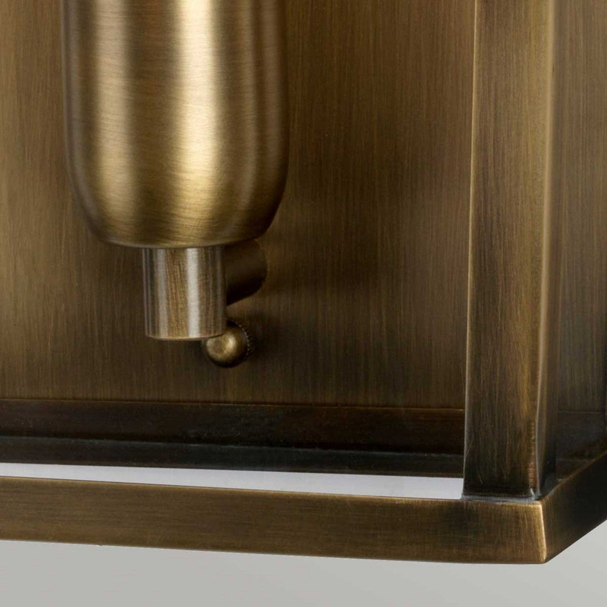 A close-up view of the Mansion 1 Light Outdoor Wall Light - Aged Brass showcases a handcrafted brass fixture with an aged finish, emphasizing its cylindrical component and rectangular base. The brushed texture on its surface gives it a timeless, antique look ideal for outdoor settings.